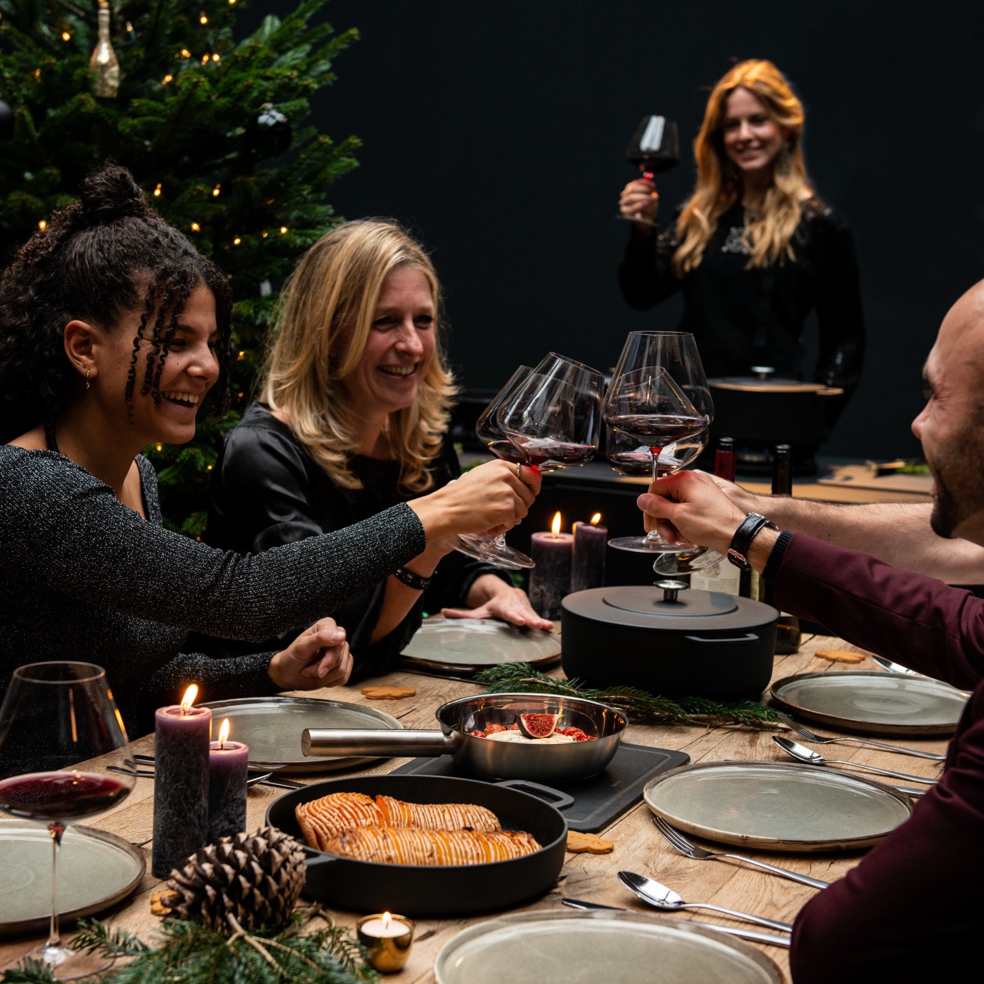 Friends celebrating around a festive dinner table with Combekk - Dutch cookware, enjoying glasses of wine and a delicious meal.