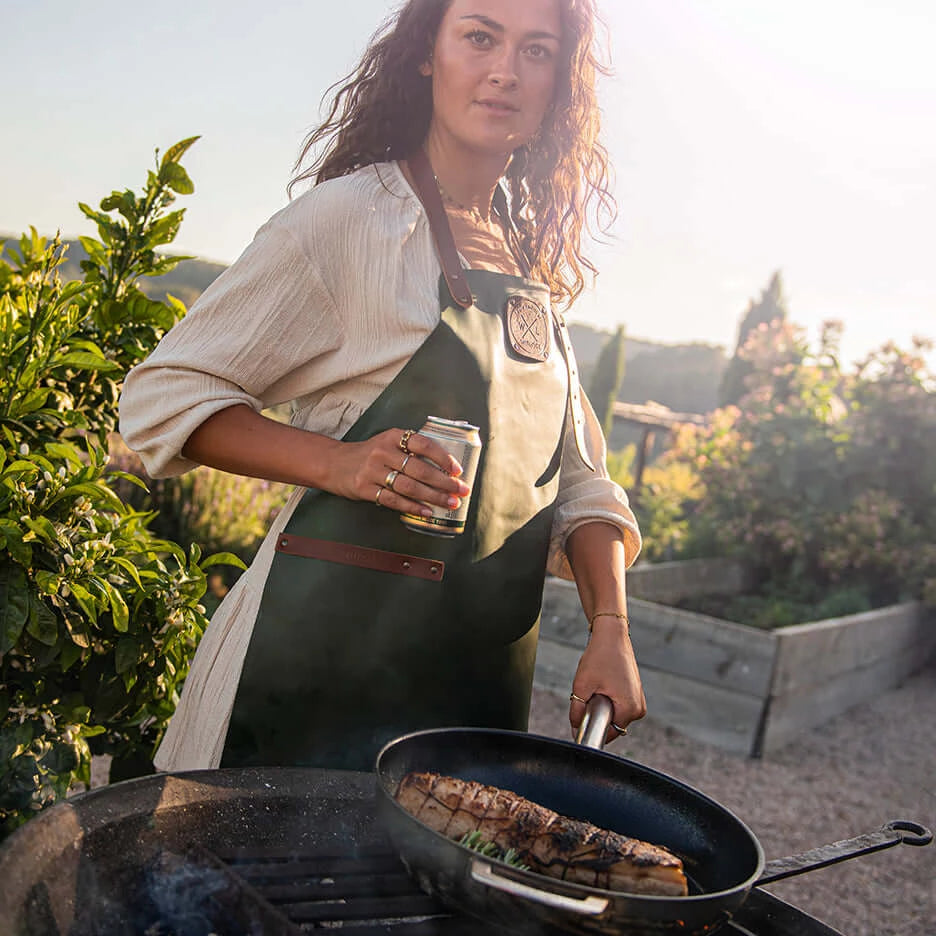 Woman wearing an apron cooking meat in a COMBEKK | Ceramic Stainless Steel Fry Pan outdoors.