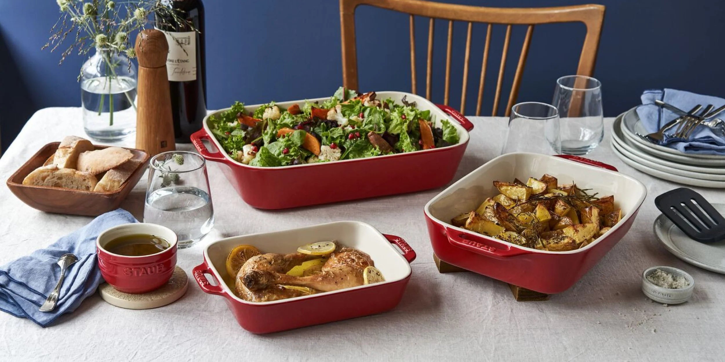 Staub Ceramic Bakeware collection featuring red baking dishes, salad, and side dishes on a dining table.