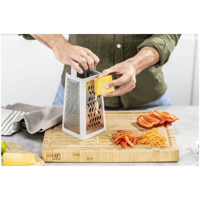 Person using a grater to shred cheese on a wooden cutting board, showcasing essential Kitchen Tools for cooking.