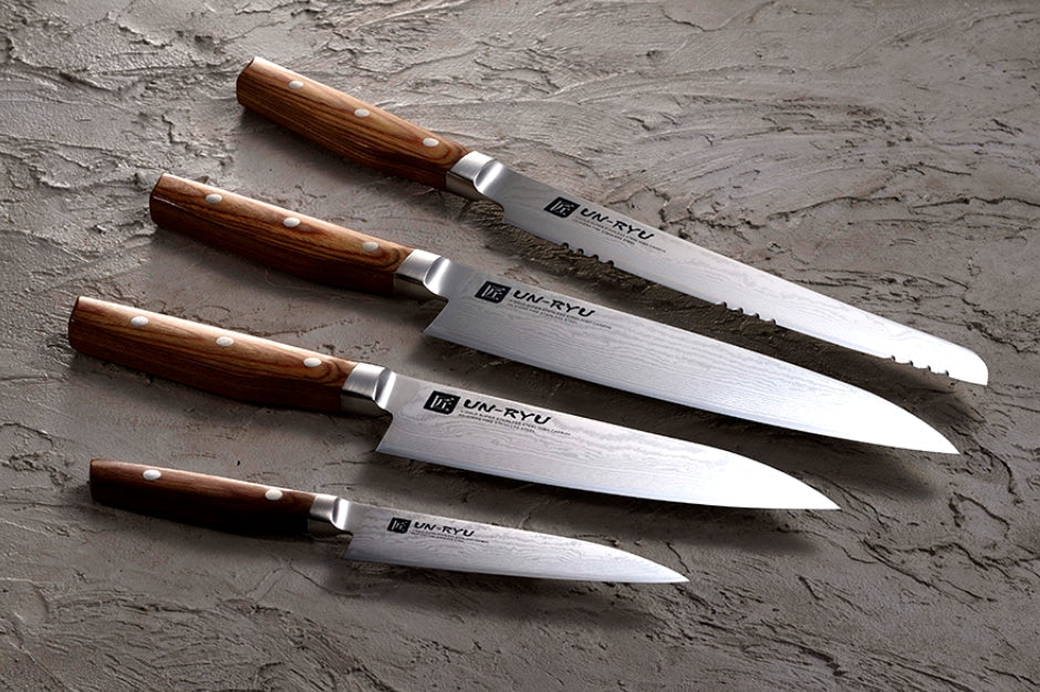 Four UN-RYU Japanese knives showcasing craftsmanship and design on a textured surface.