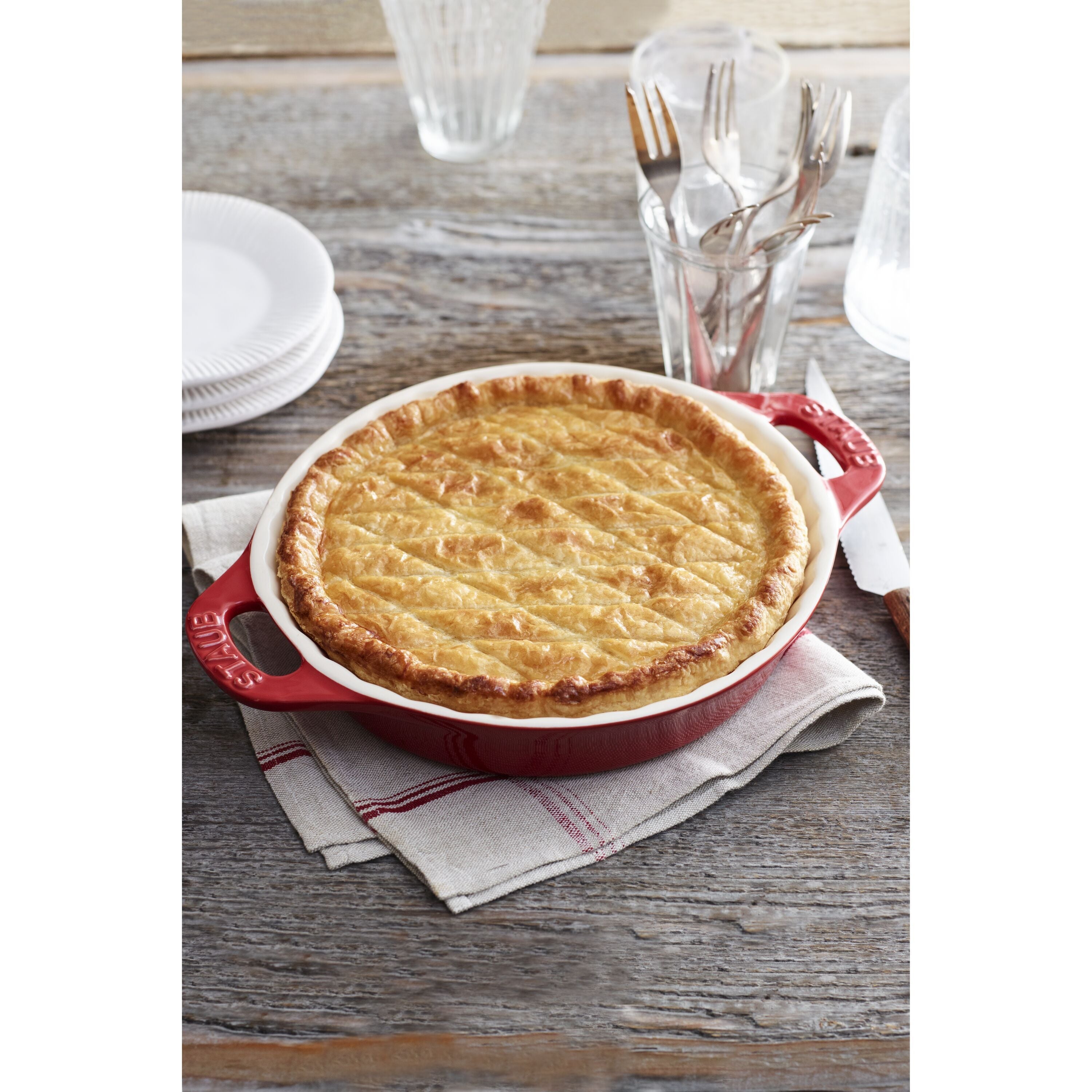 Pie in a STAUB Ceramique Ceramic Round Pie Dish on a wooden table with cutlery and plates.