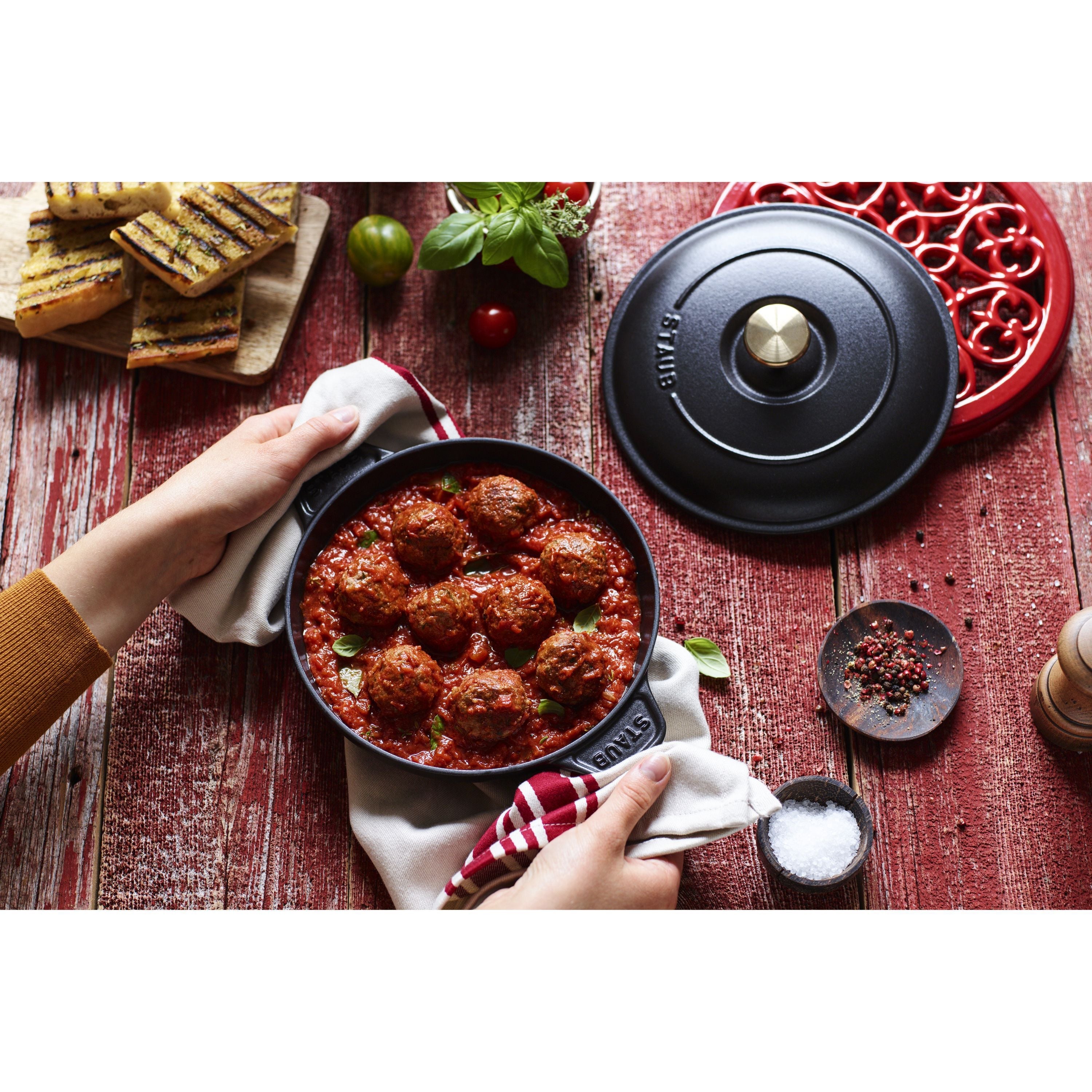 STAUB Specialities 750 ml Cast Iron Round Oven Dish with Lid, Black holding meatballs in sauce on a rustic table.