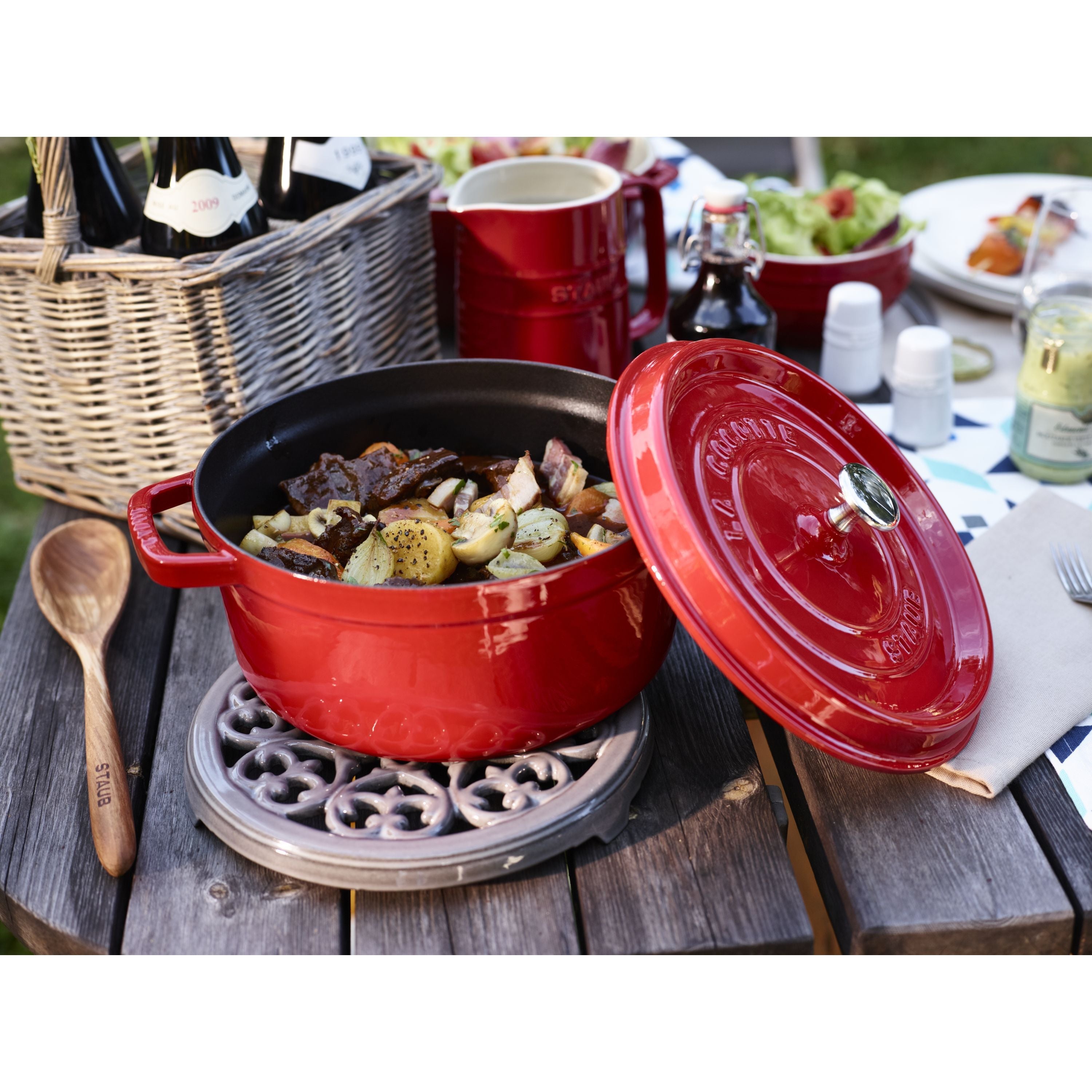 Red pot on STAUB Serving Round Cast Iron Trivet, Lily Decal, Graphite-Grey on wooden table outdoors.