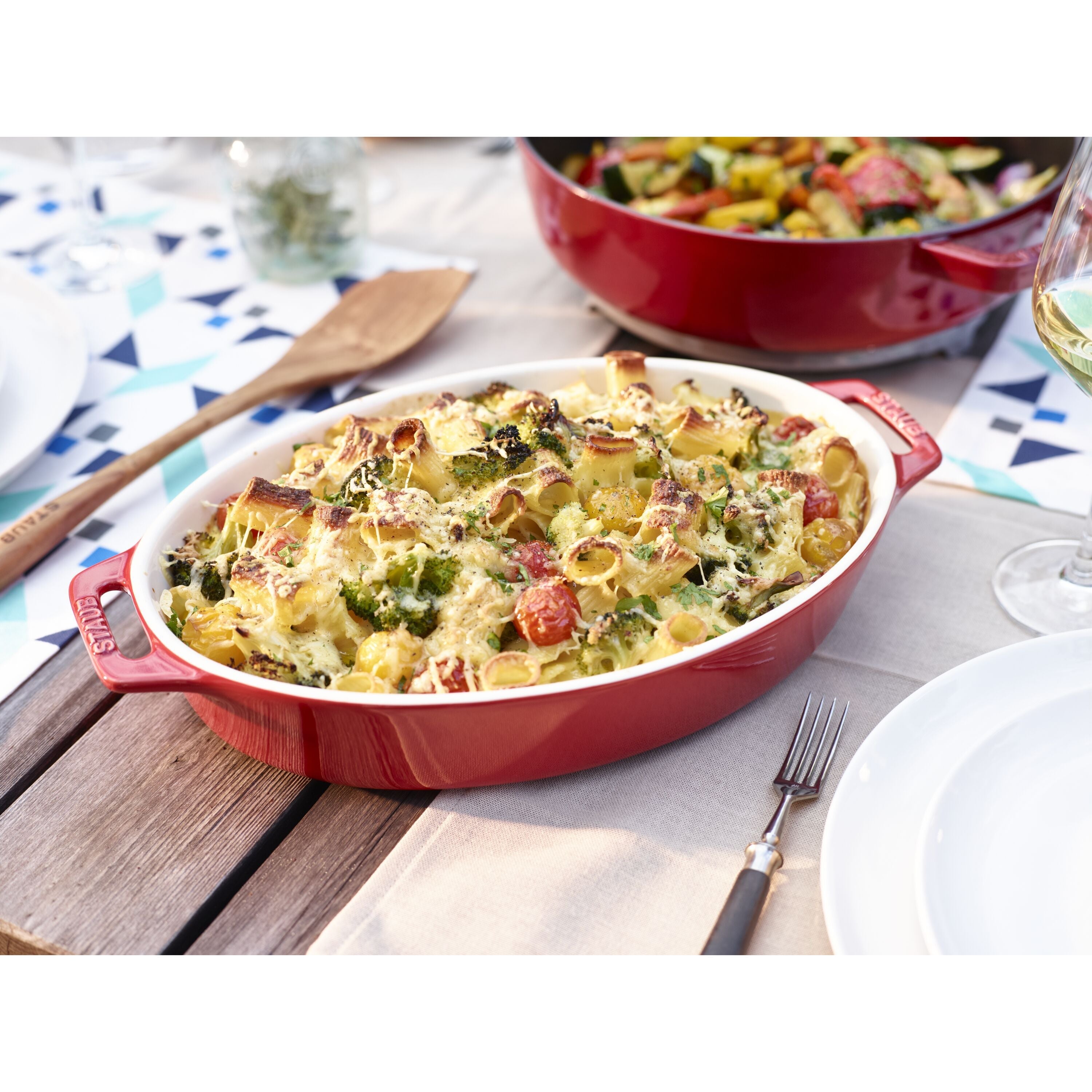 Red STAUB Ceramique Ceramic Oval Oven Dish with a baked pasta dish on a wooden table.