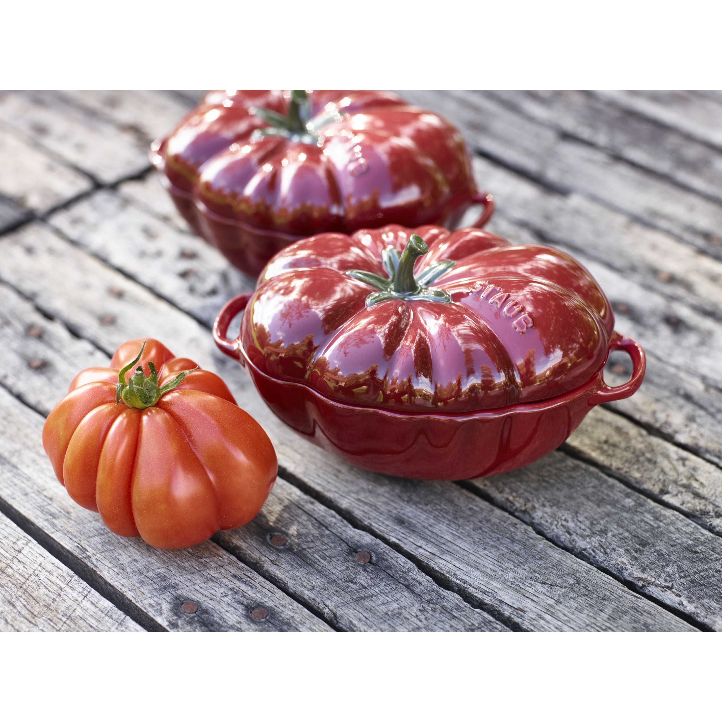 STAUB Ceramique Ceramic Tomato Cocotte displayed with a Brandywine tomato on a rustic wooden table.