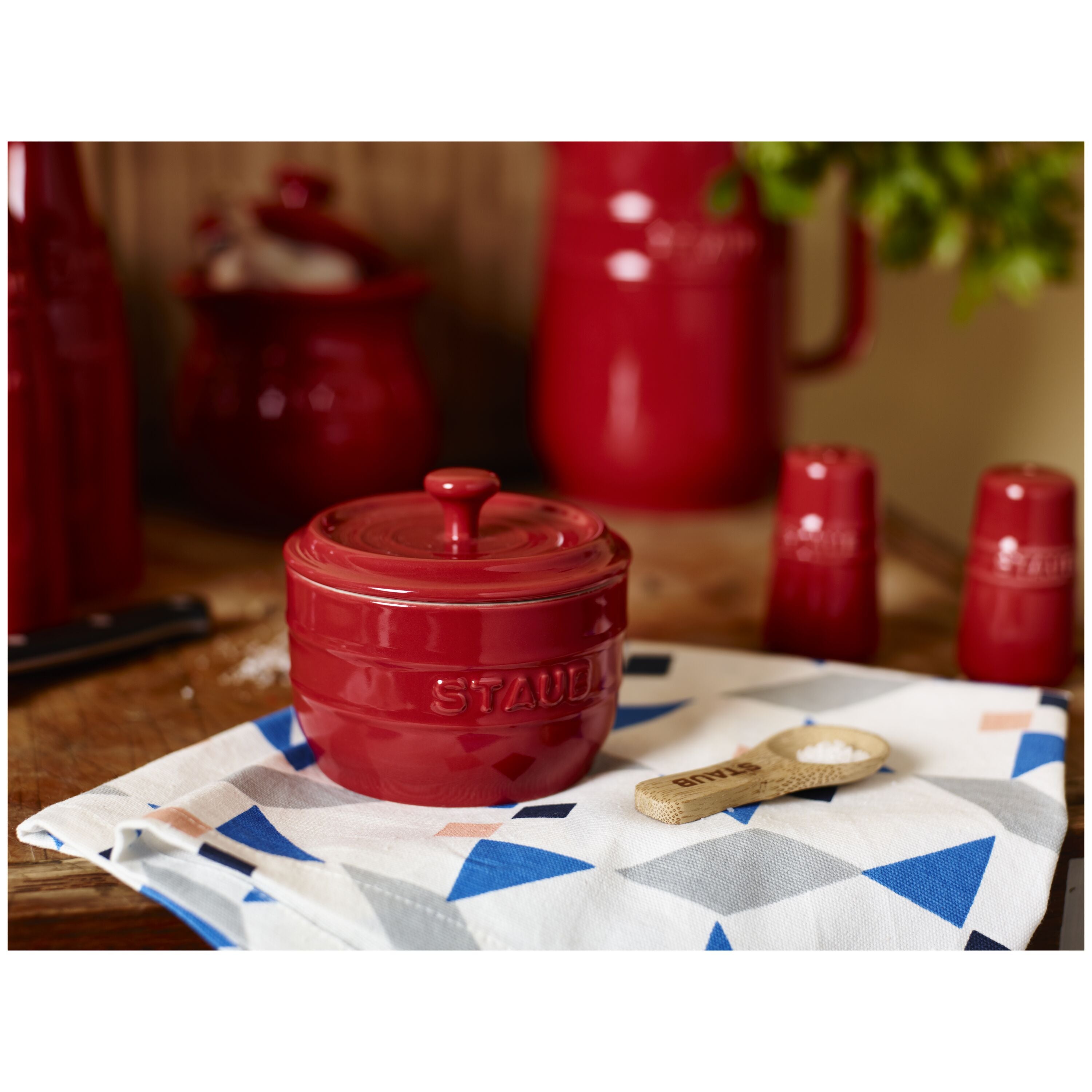 STAUB Ceramique Ceramic Salt Crock on a patterned cloth with kitchen setting in the background