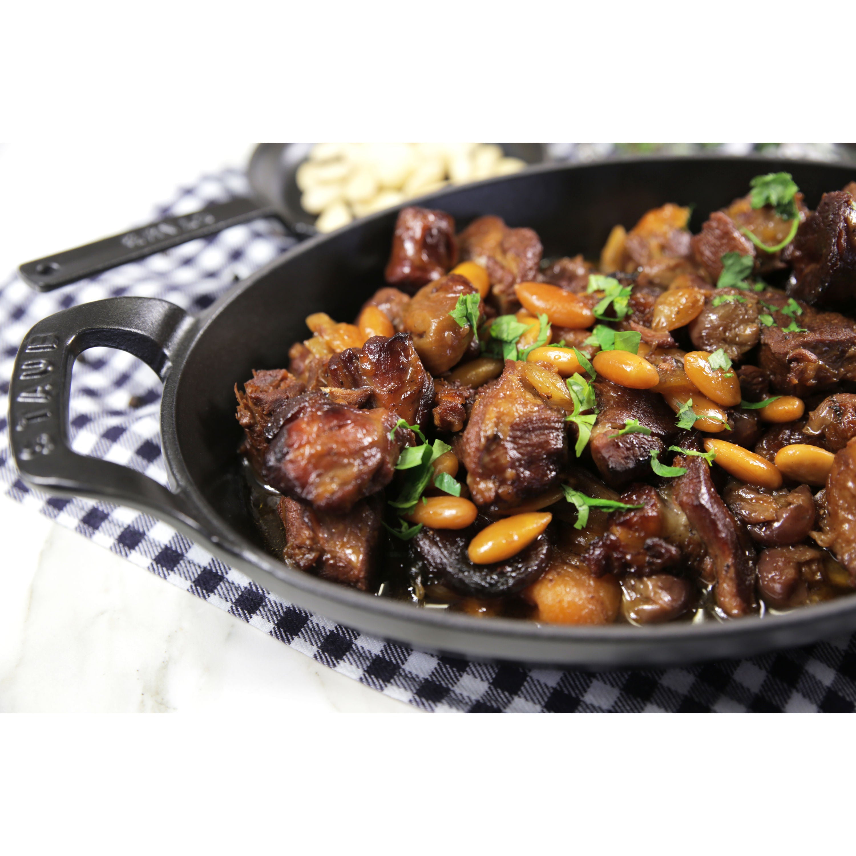 Stewed dish with beans and mushrooms in a black cast iron skillet on a checkered tablecloth.