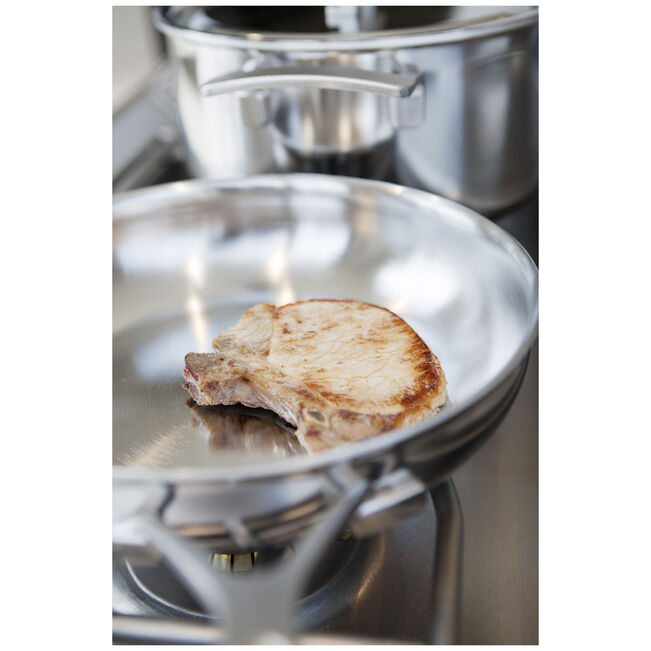 Stainless steel pan with a piece of meat on a stove