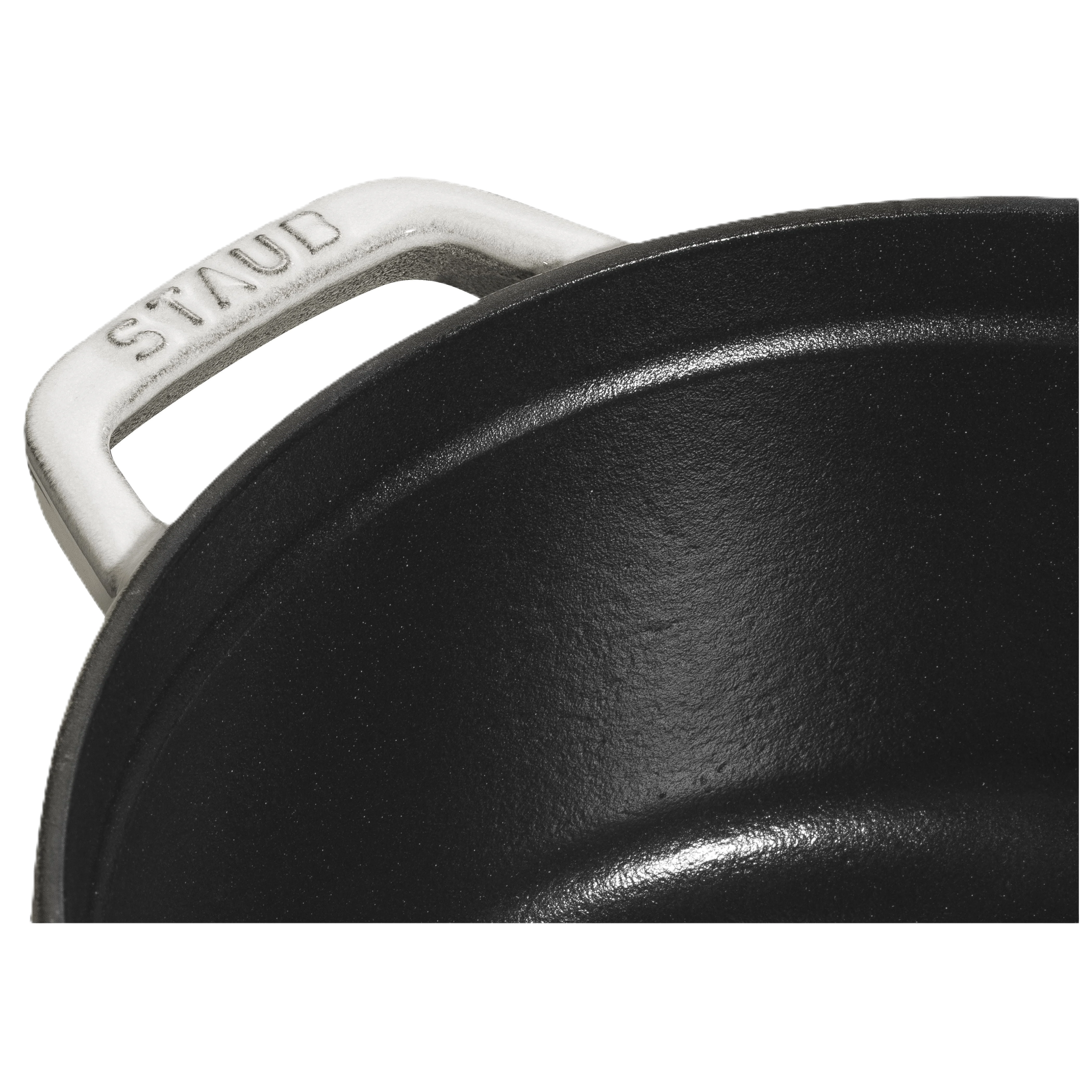 Close-up of a black cast iron skillet with a white handle, featuring the Staub logo.