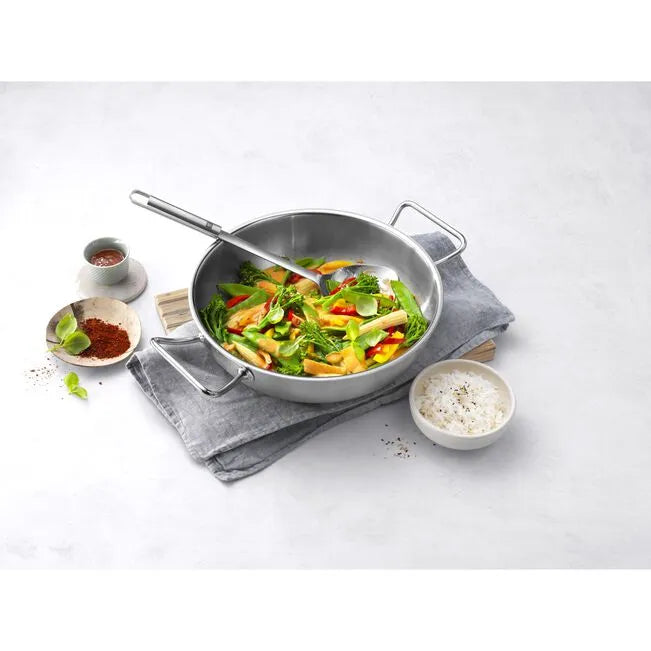 Stainless steel wok with stir-fried vegetables on a white surface