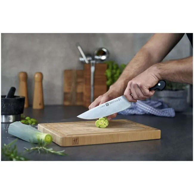 Chef using ZWILLING Pro Knife Set 3 Piece on a wooden cutting board to slice vegetables in a kitchen setting.