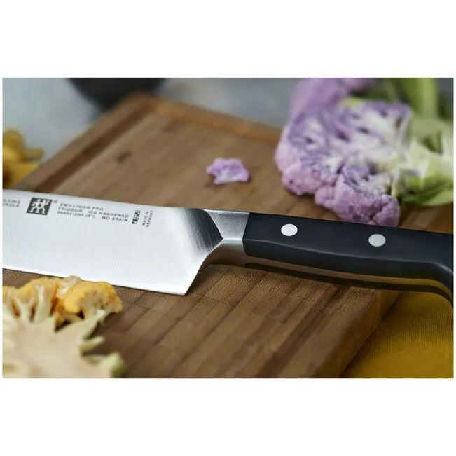Knife on a wooden cutting board with vegetables in the background