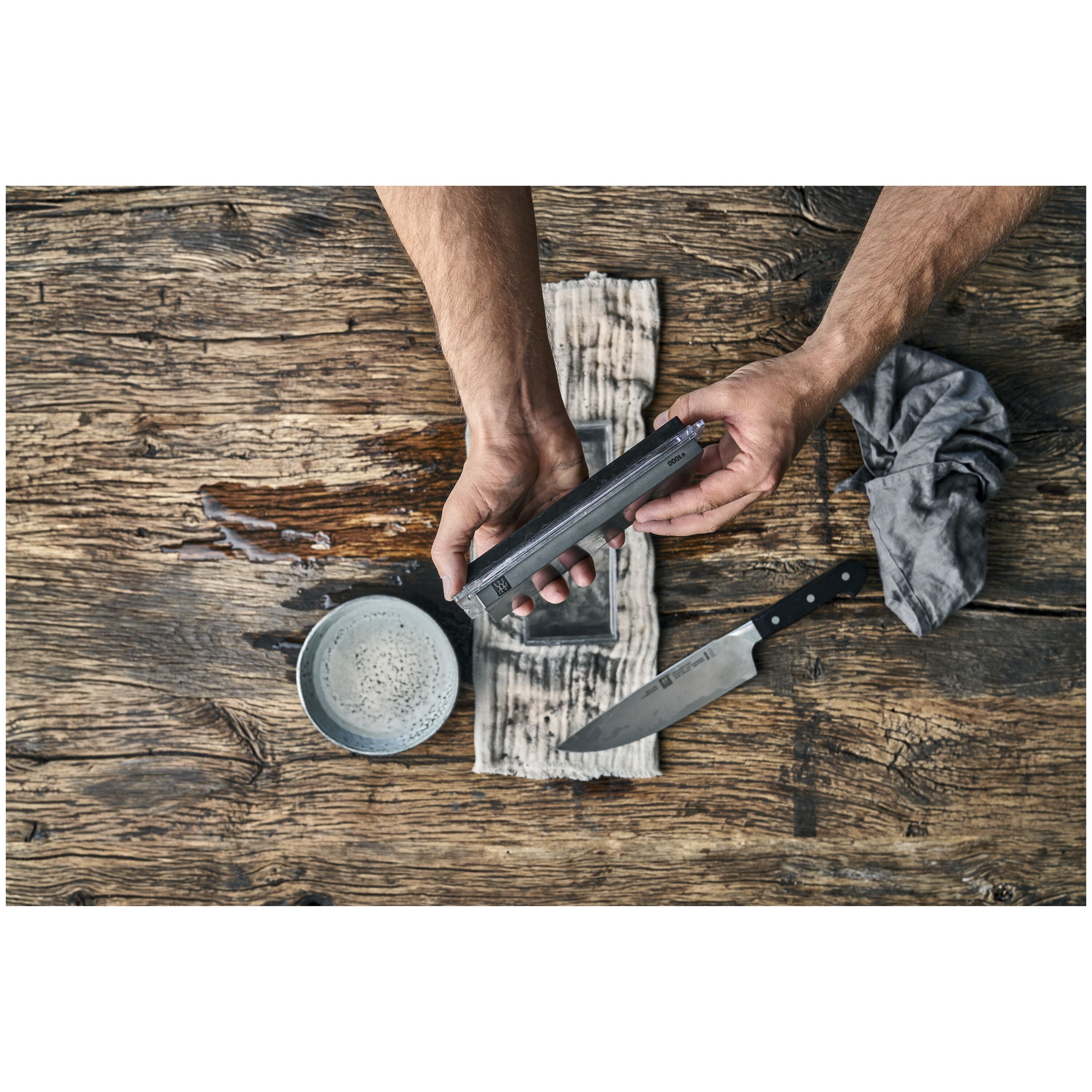 ZWILLING Sharpening Stone, Pure-White being used with a knife and a bowl on a wooden countertop.