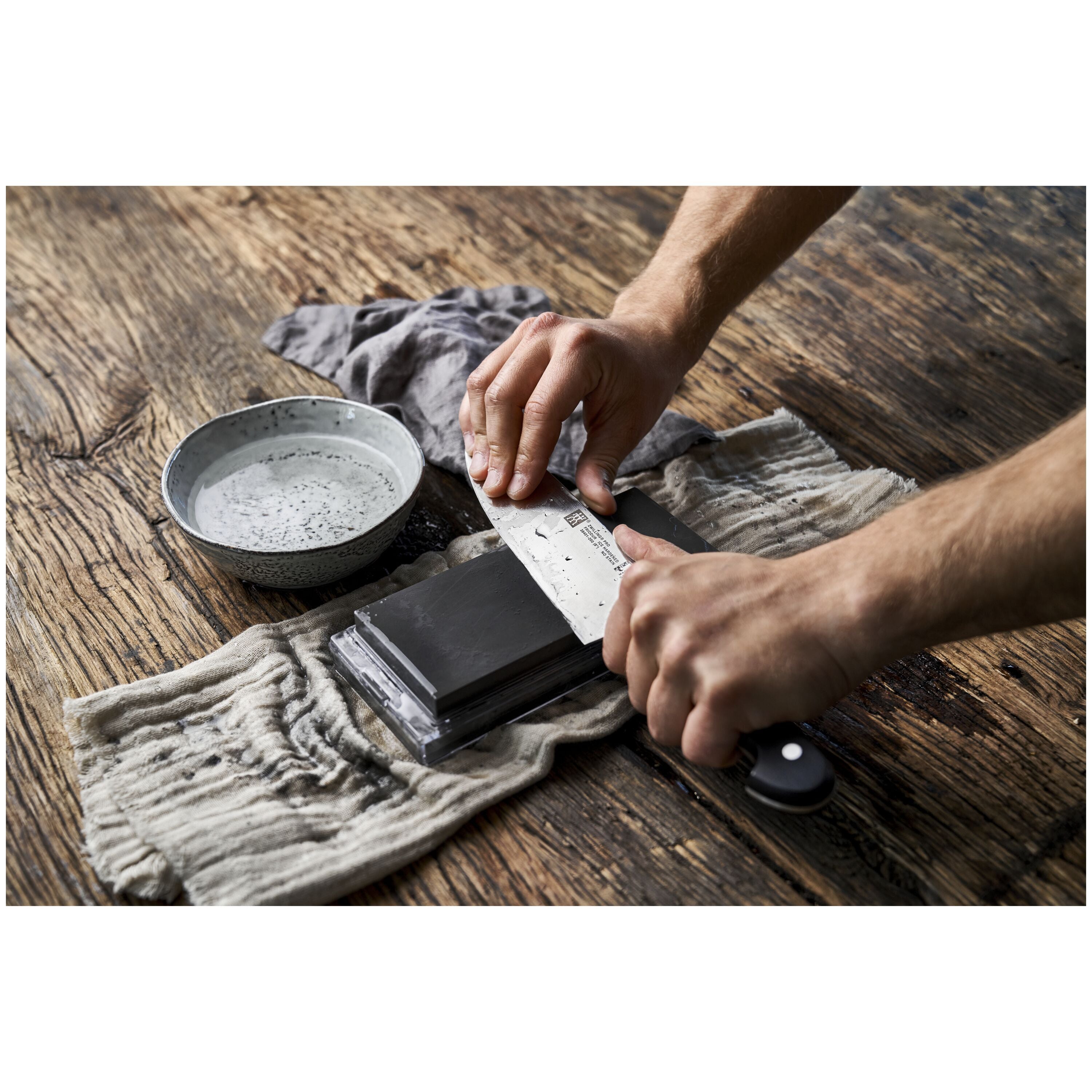 ZWILLING Sharpening Stone, Pure-White used on a knife for sharpening on a wooden surface with water bowl.