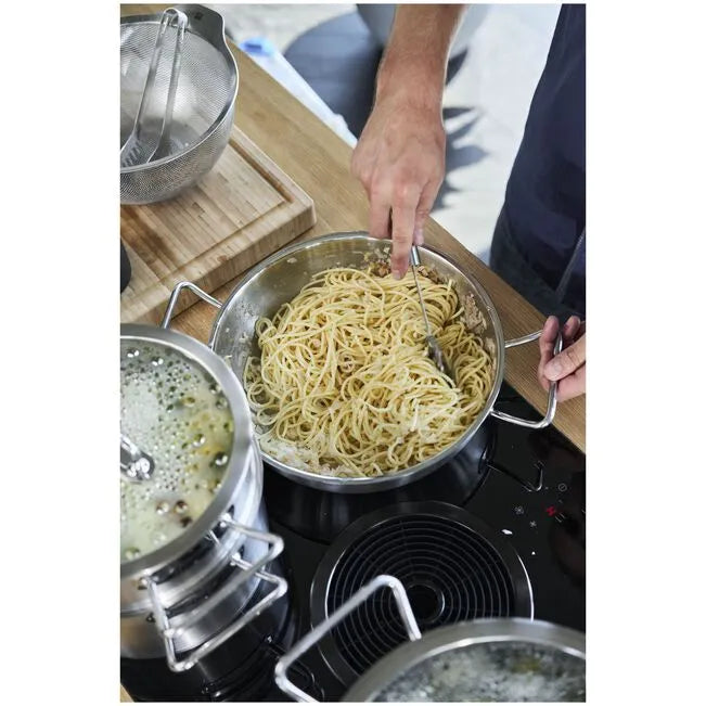 Person cooking spaghetti in a pan on a stove with a kitchen setting in the background.