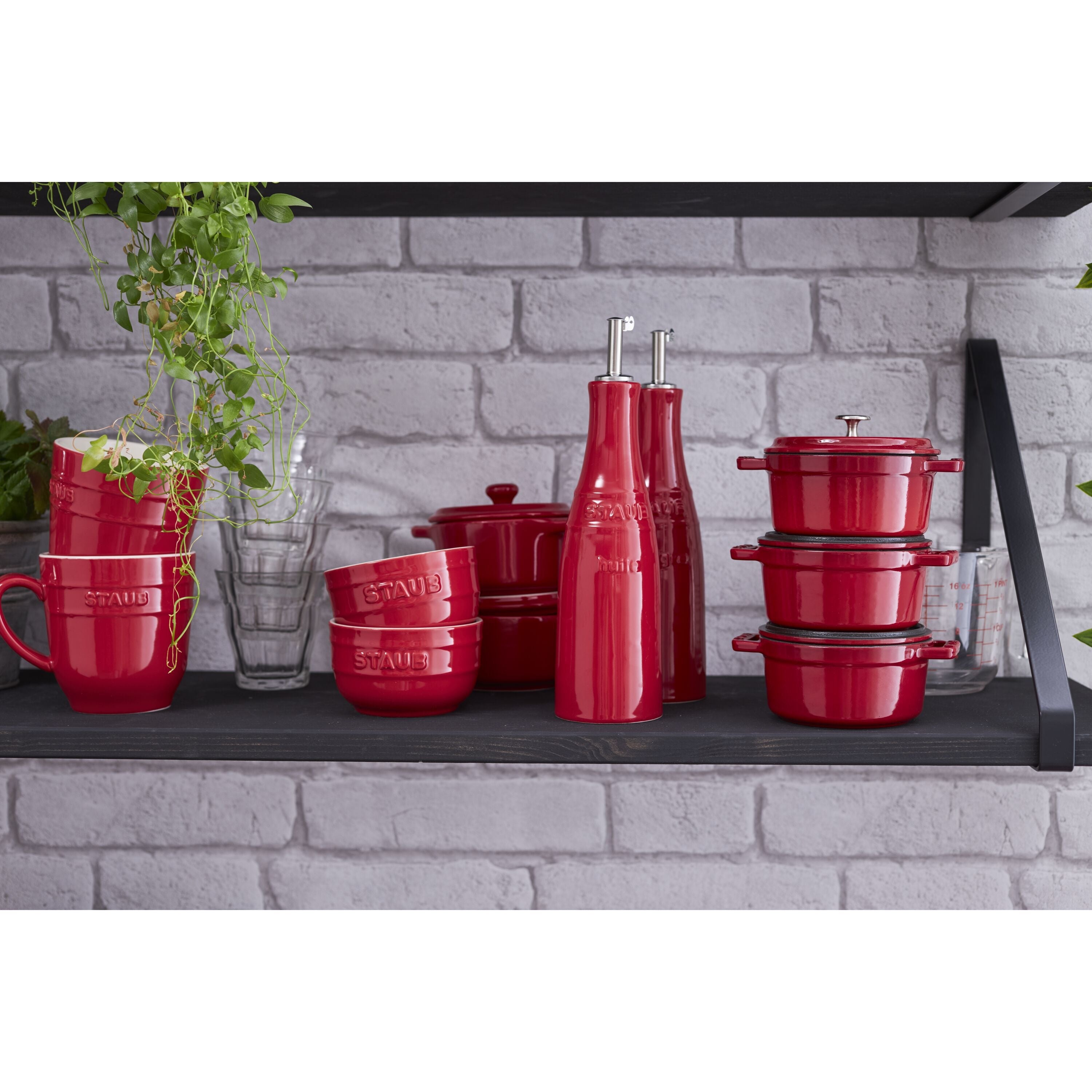 STAUB Ceramique Ceramic Oil And Vinegar Set among red cookware and glassware on a rustic shelf.