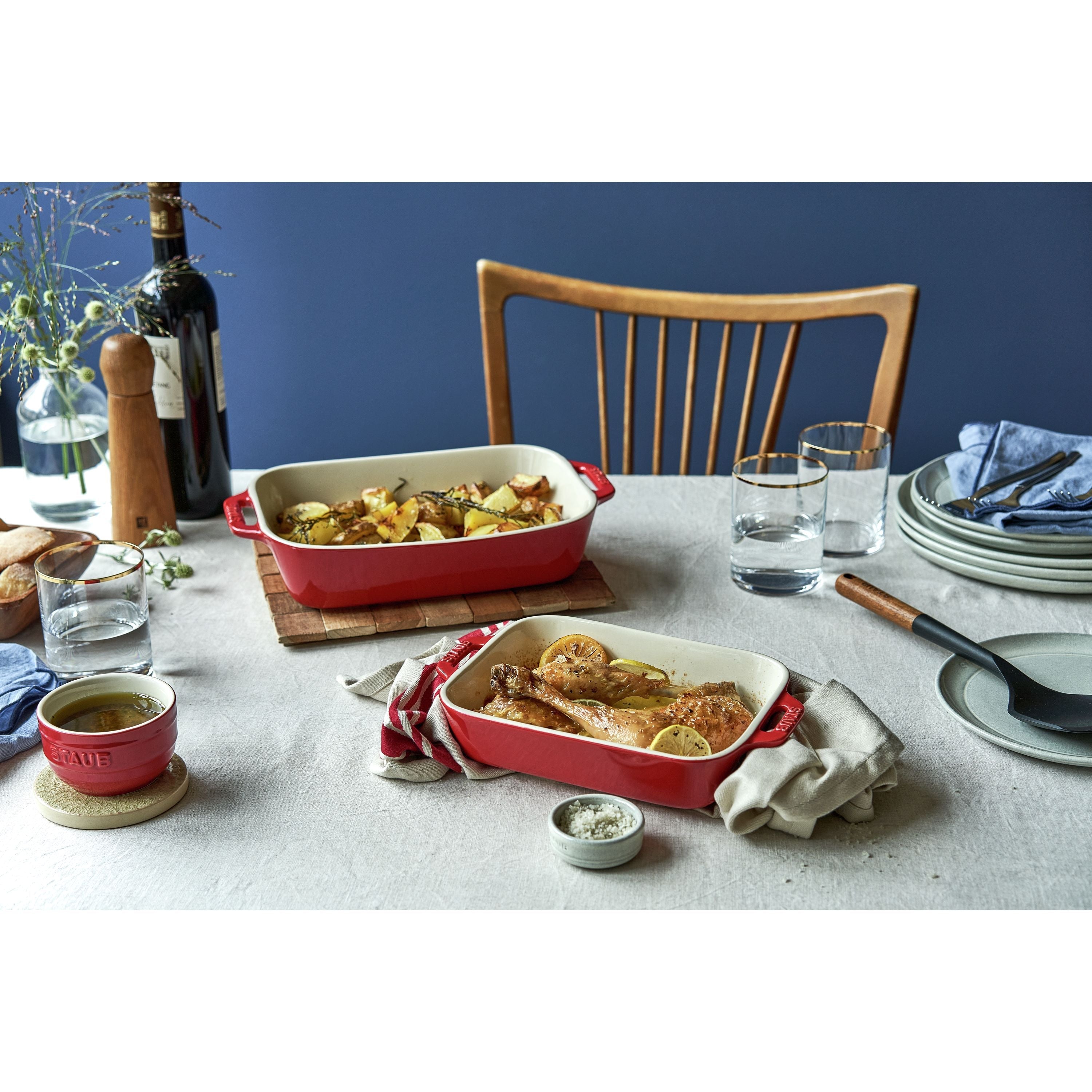 Dining table set with red ceramic dishes containing food, glasses, and a bottle of wine.