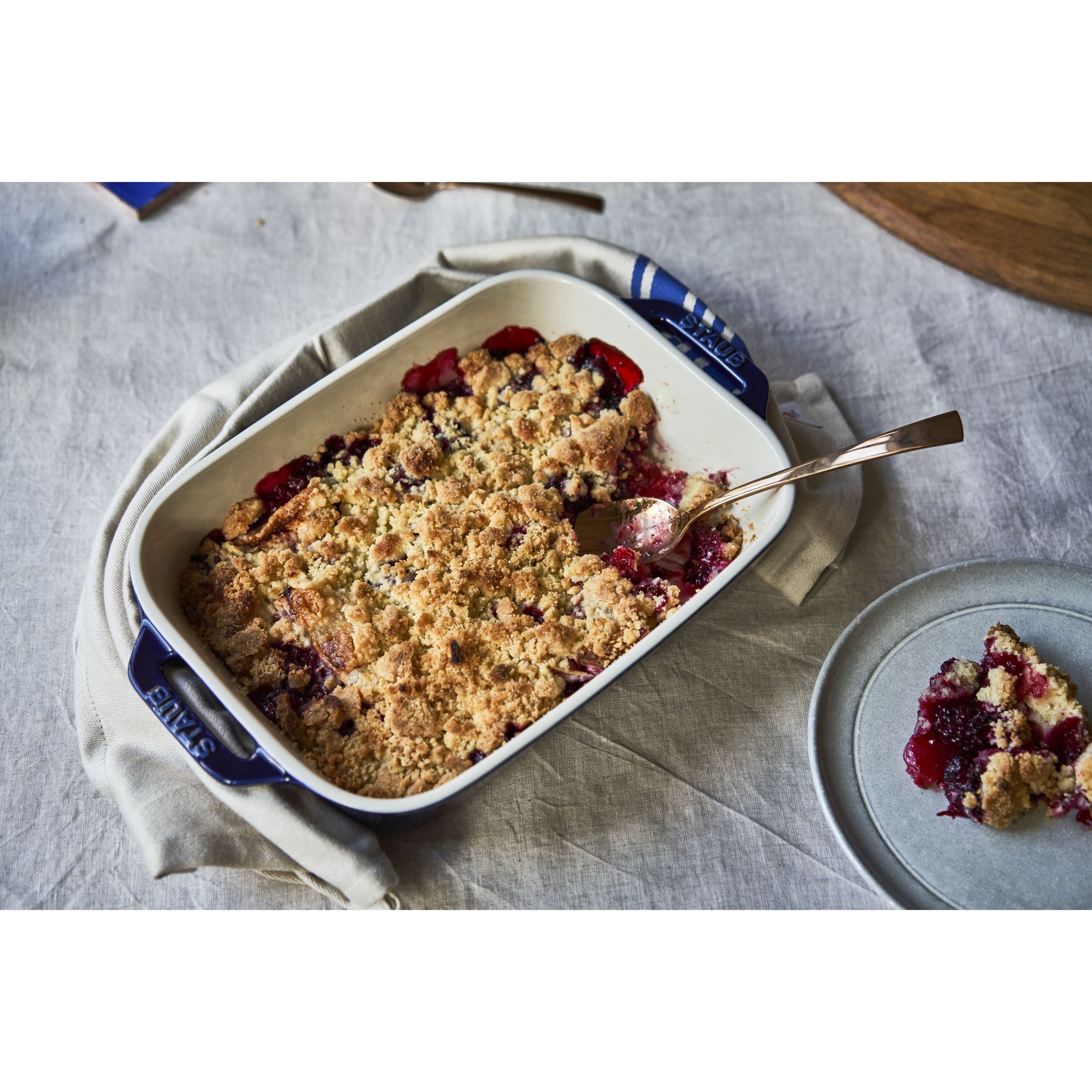 Baked dessert with crumble topping in a white dish on a tablecloth.