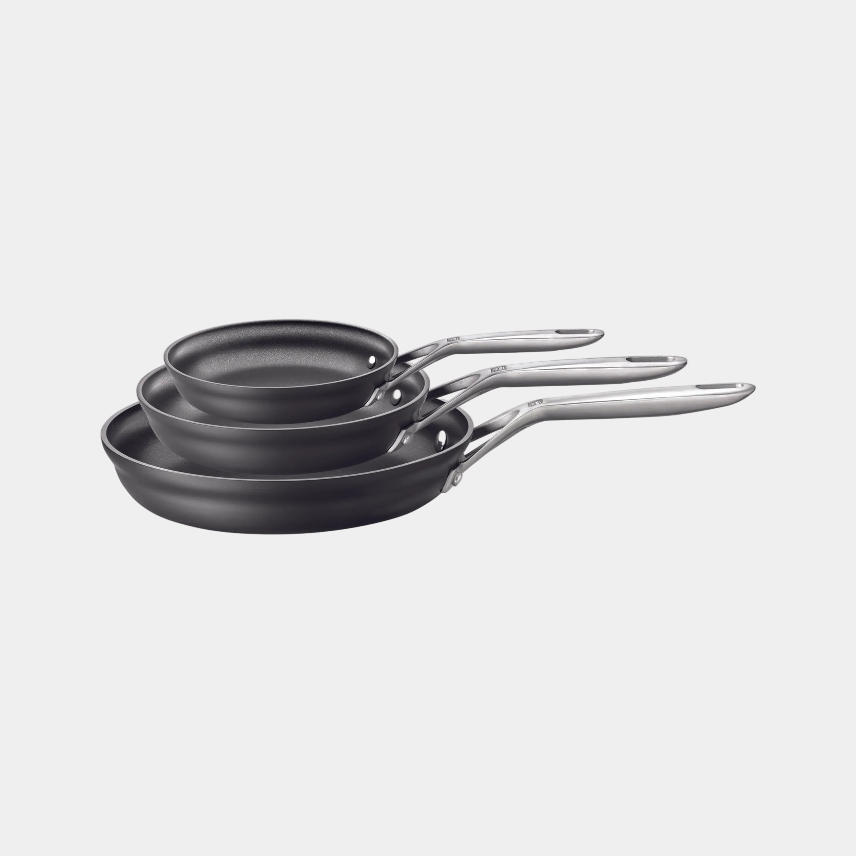 Set of three black frying pans with silver handles on a white background