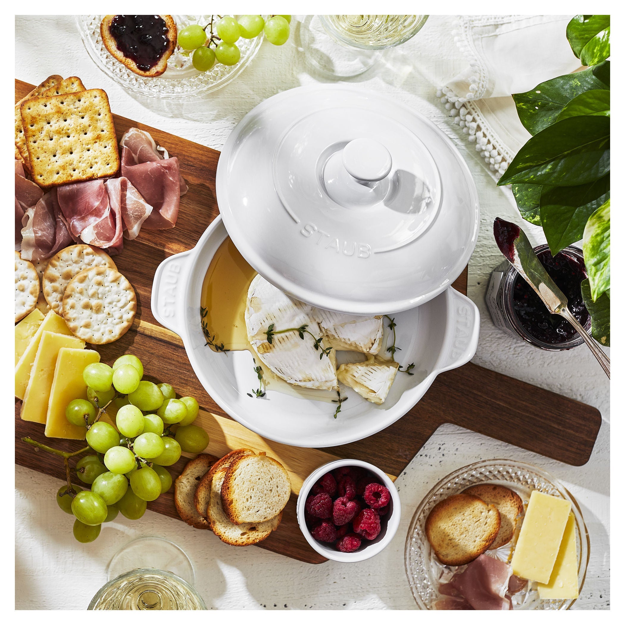 Assorted appetizers including cheese, crackers, and fruits on a table with a white ceramic dish.