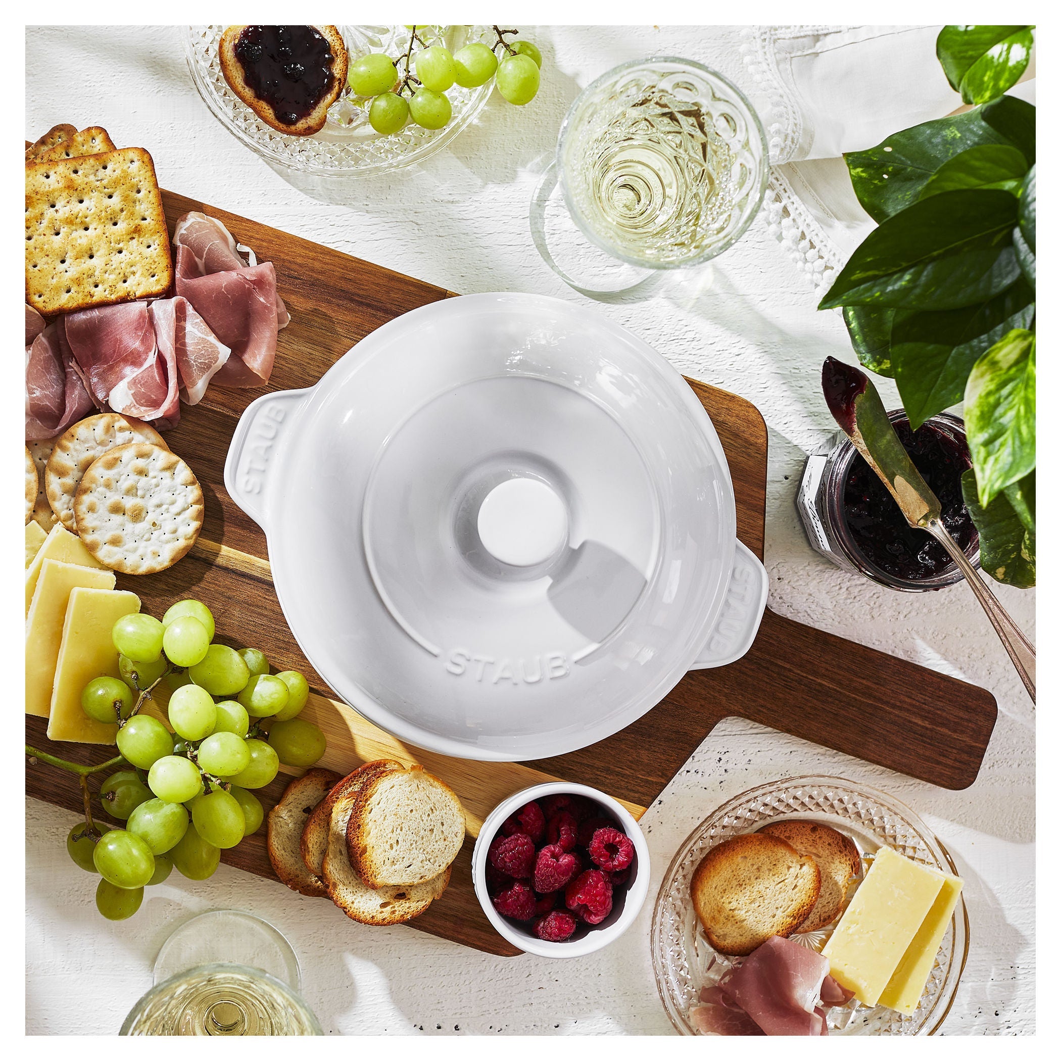 White ceremic dish on a wooden board with food items and glasses.