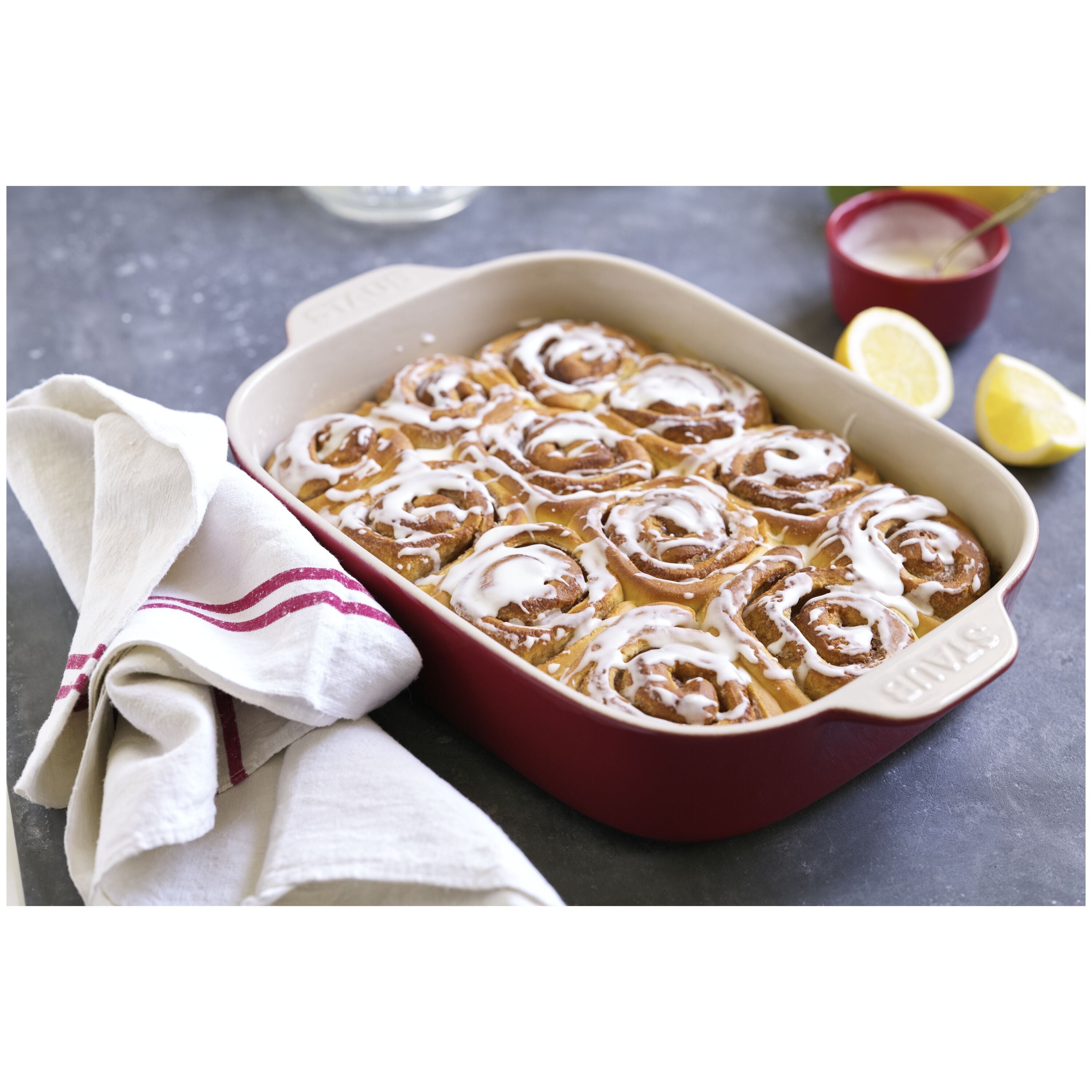 STAUB Ceramique Ceramic Rectangular Oven Dish filled with cinnamon rolls, placed on a dark countertop with a towel.