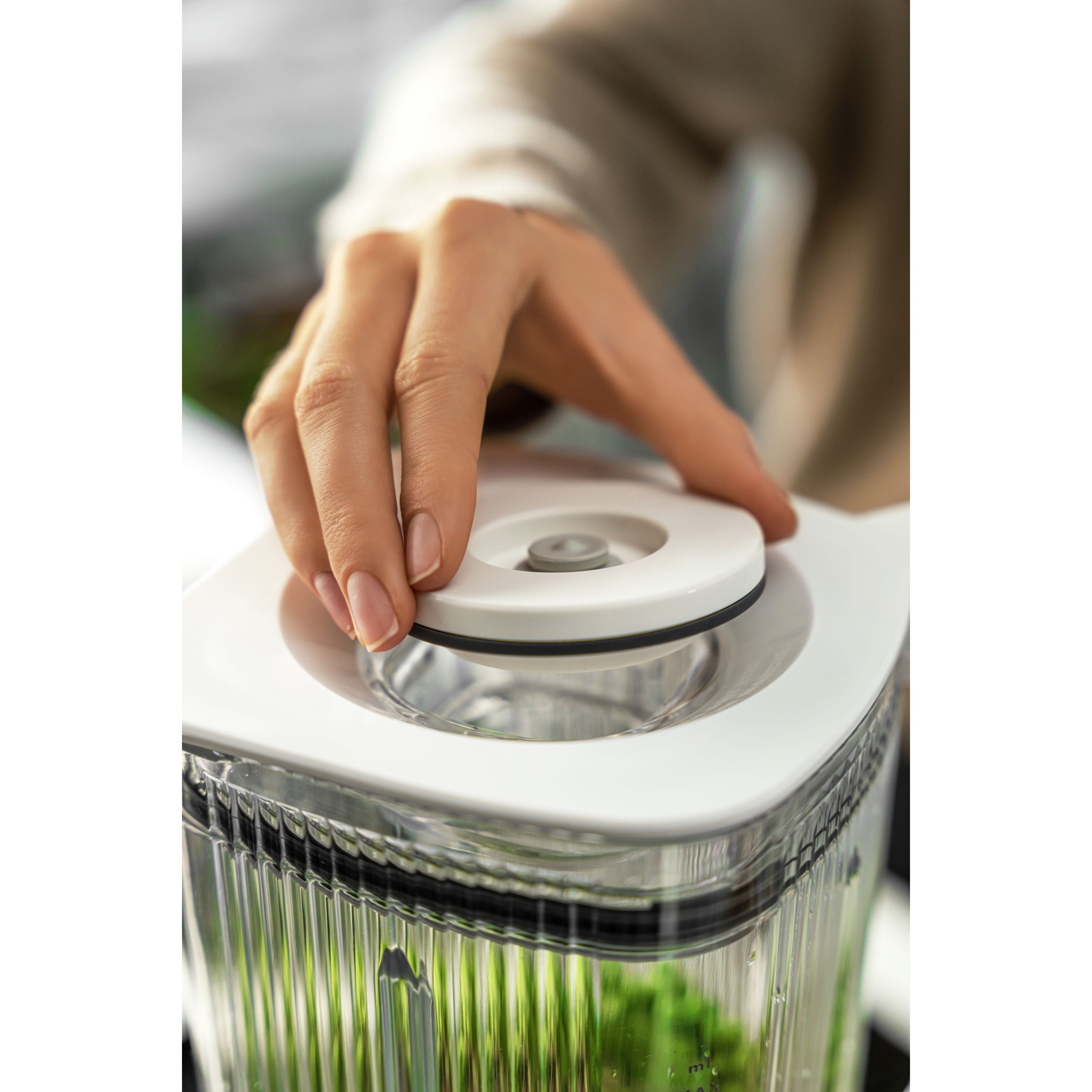 Hand using a salad spinner with fresh greens on a white background
