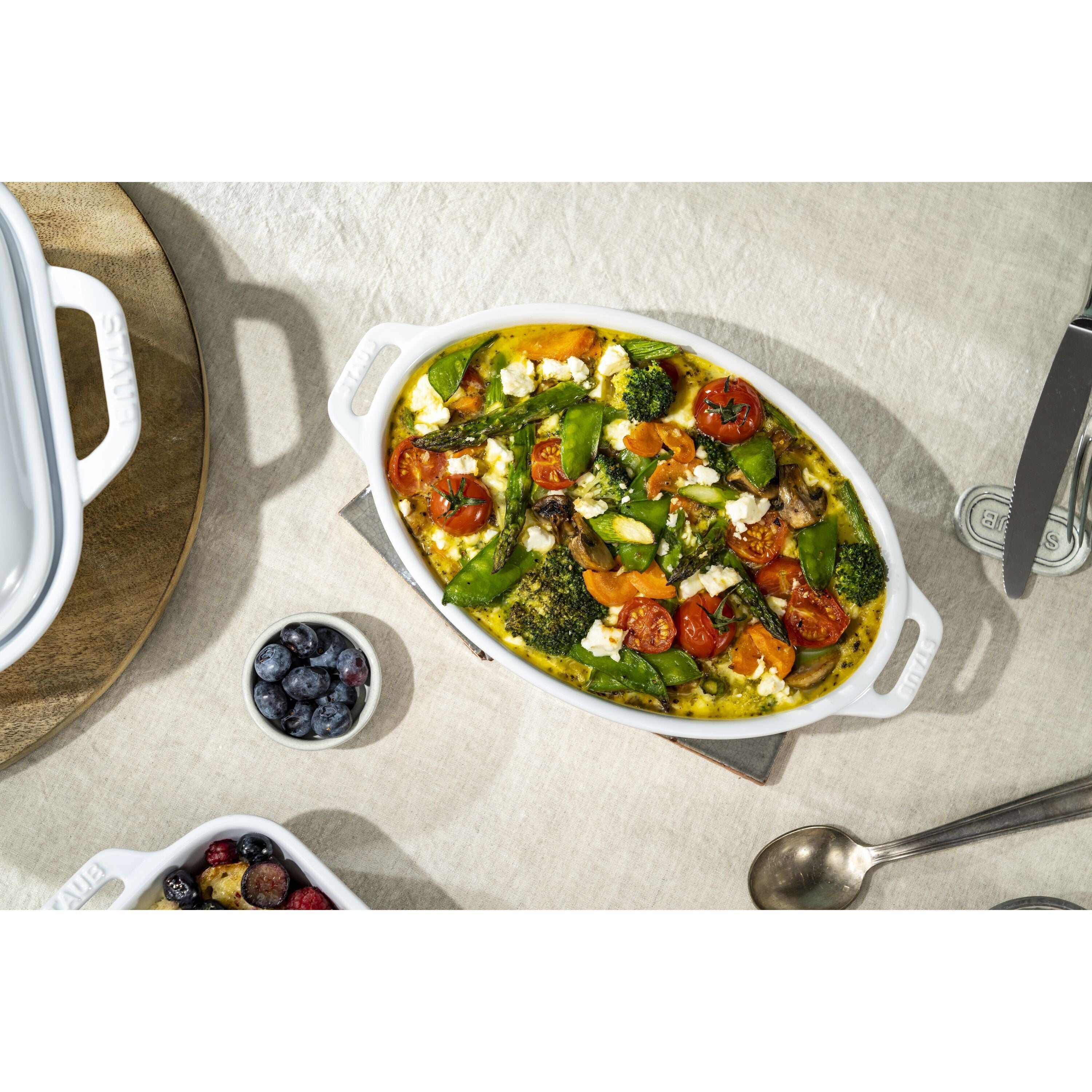 Vegetarian dish with tomatoes and greens in a white oval dish on a beige surface.
