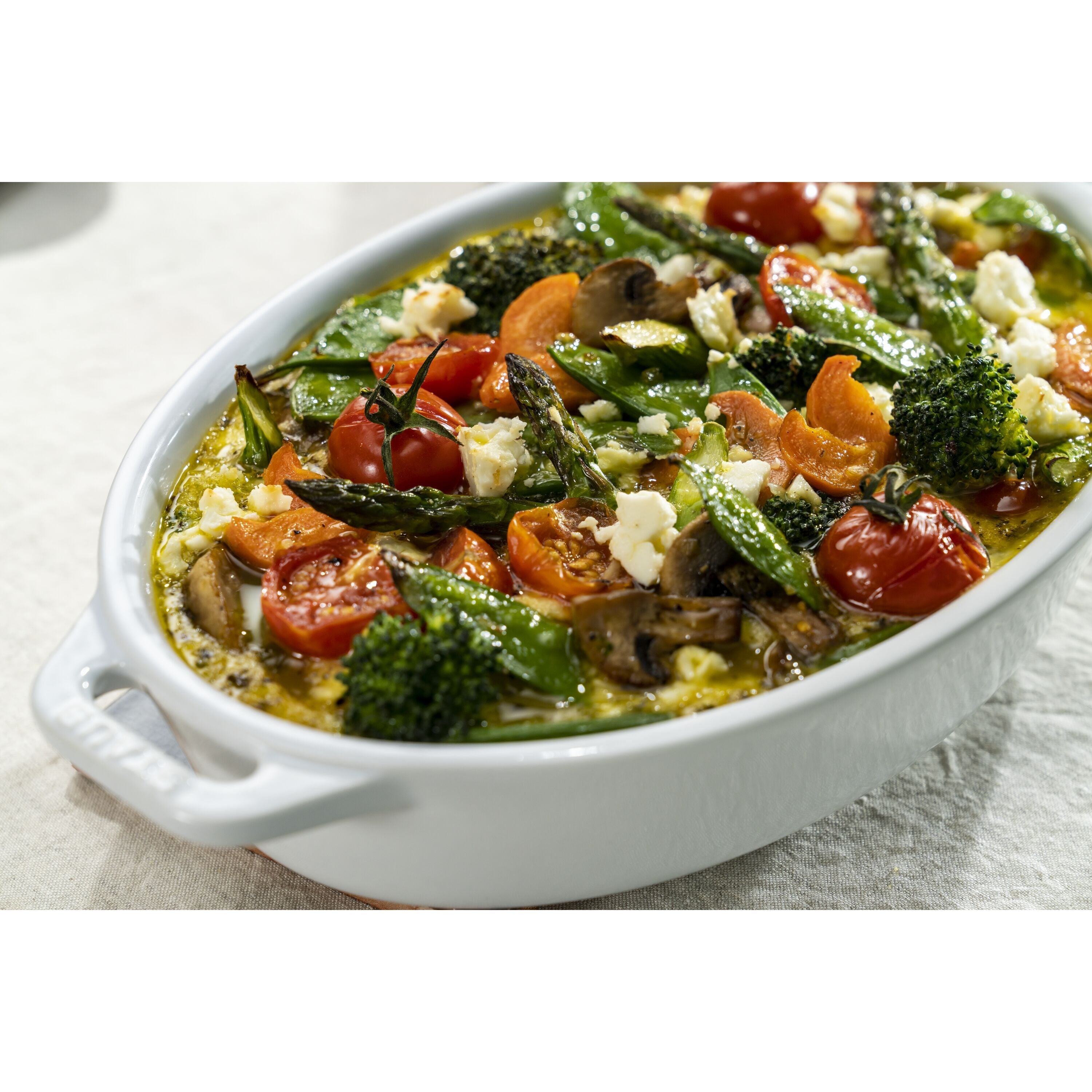 Vegetable dish with asparagus, tomatoes, and feta cheese in a white oval dish on a light background