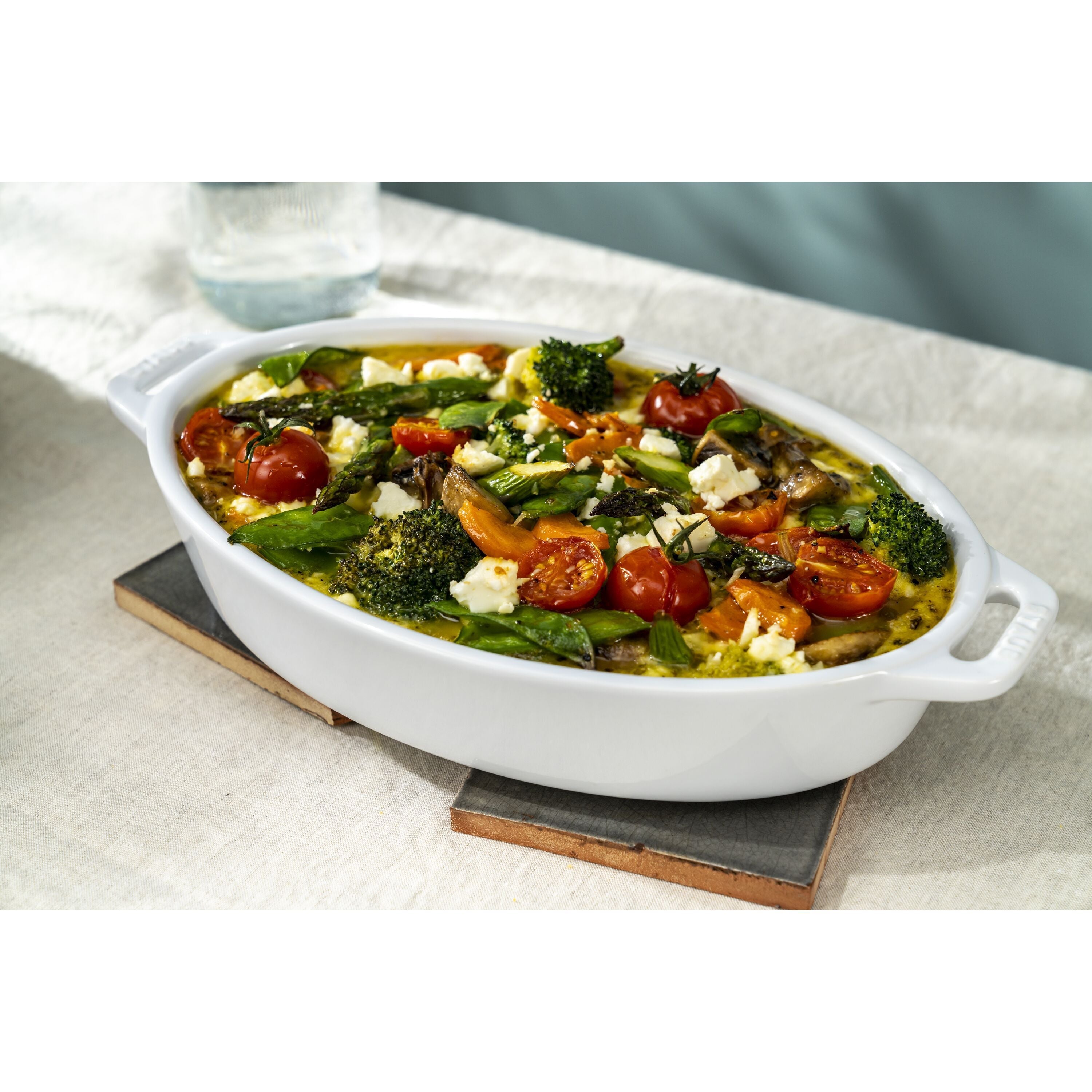 White oval dish filled with a vegetable and feta casserole on a light background