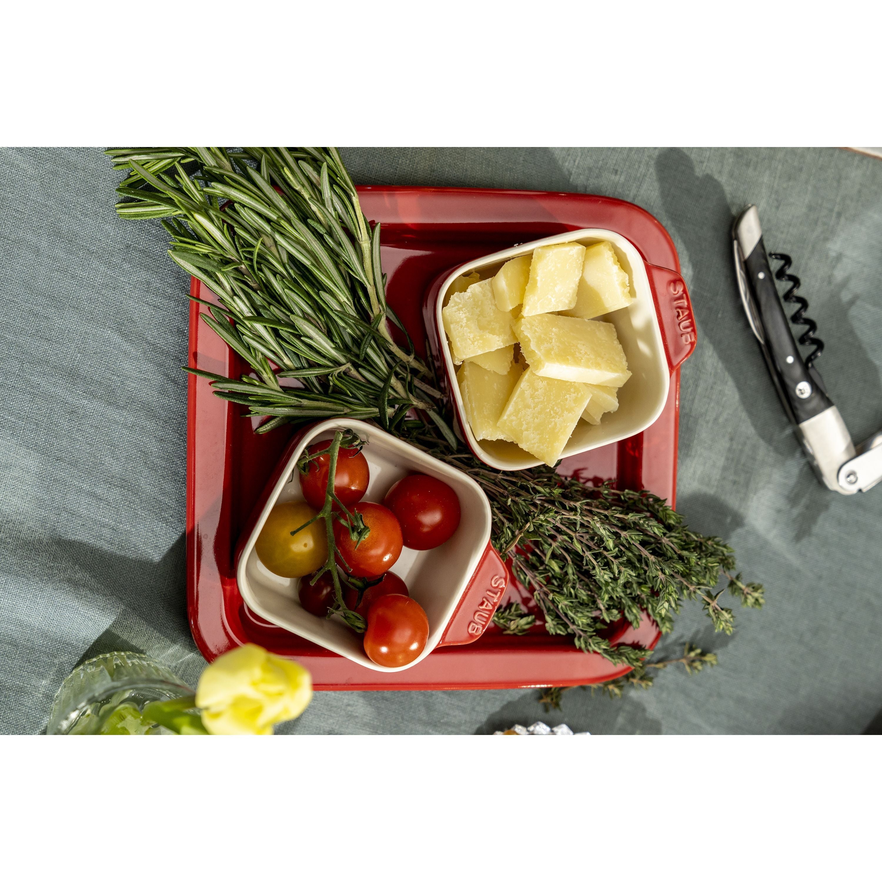 Red Staub dish with cheese, tomatoes, and herbs on a gray surface