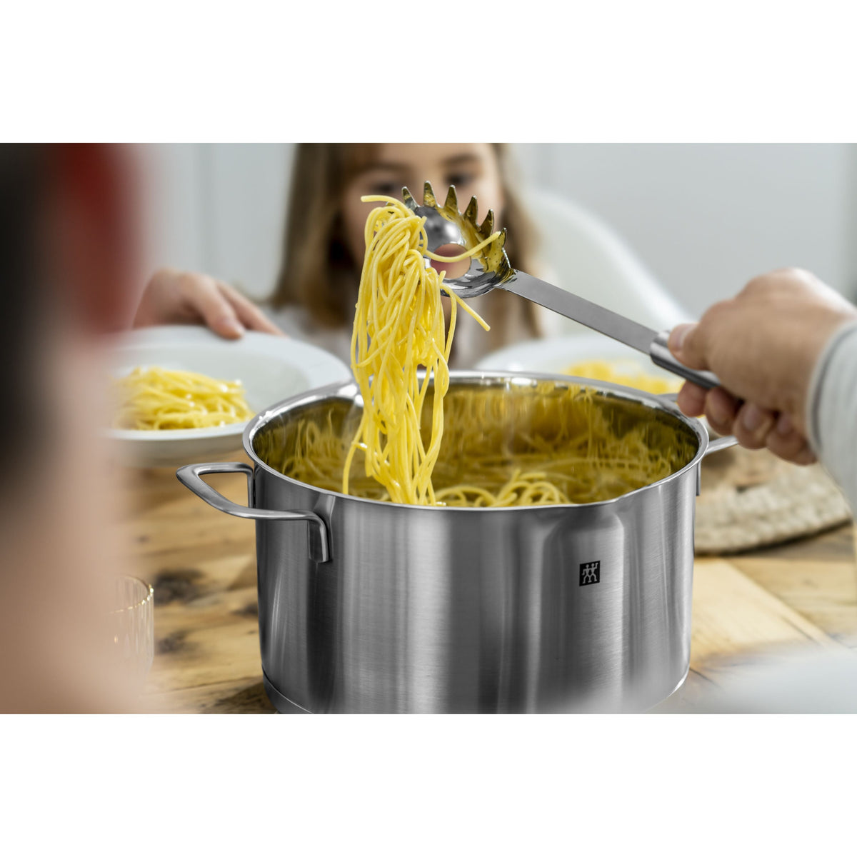 Stainless steel pot with pasta being served, blurred background