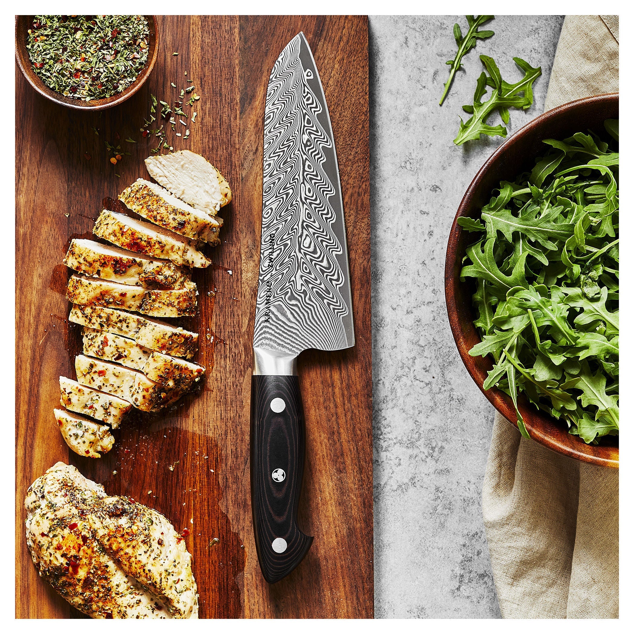Chef's knife on a wooden cutting board with sliced chicken and fresh arugula.