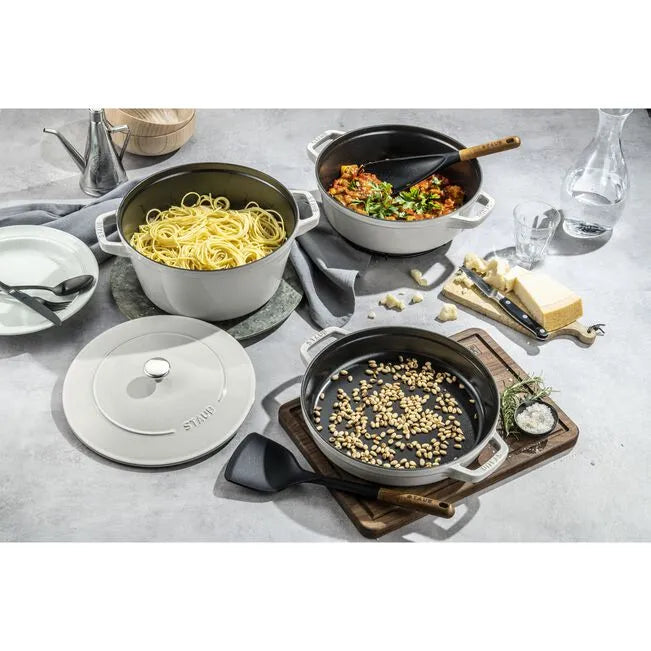Stainless steel cookware set on a gray surface with food items.