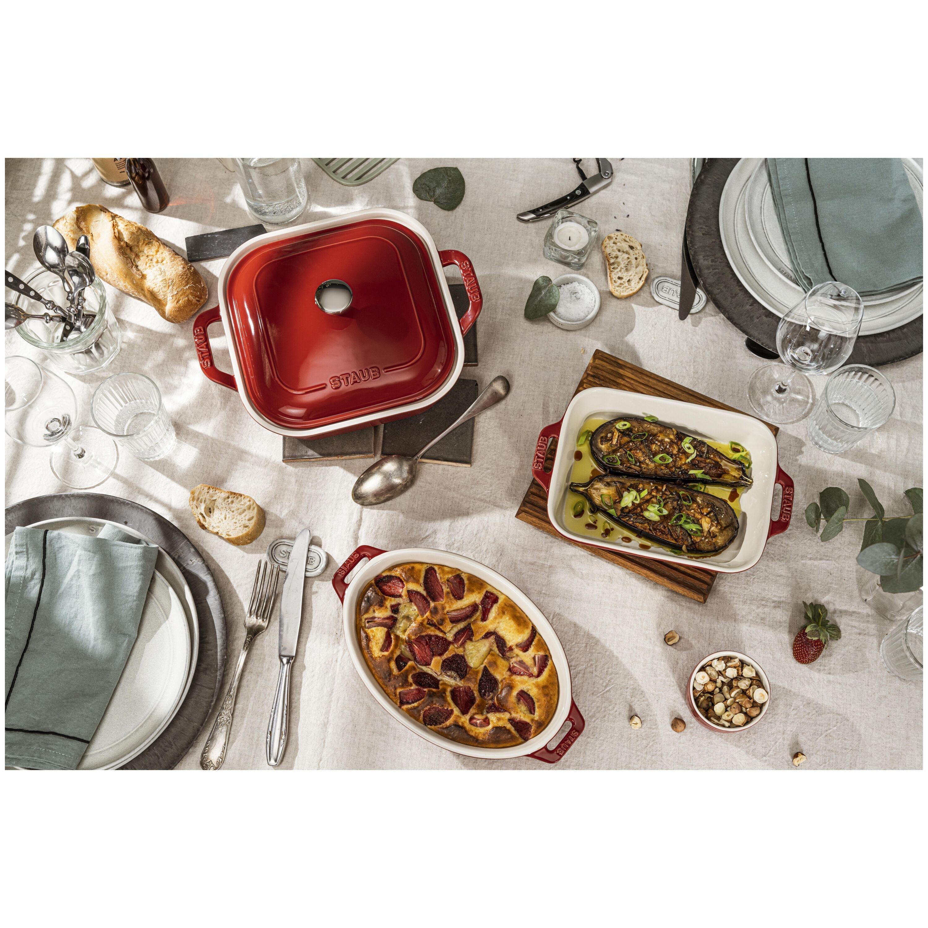 Dining table set with STAUB Ceramique Ceramic Oval Oven Dish, food, and tableware on a white tablecloth.