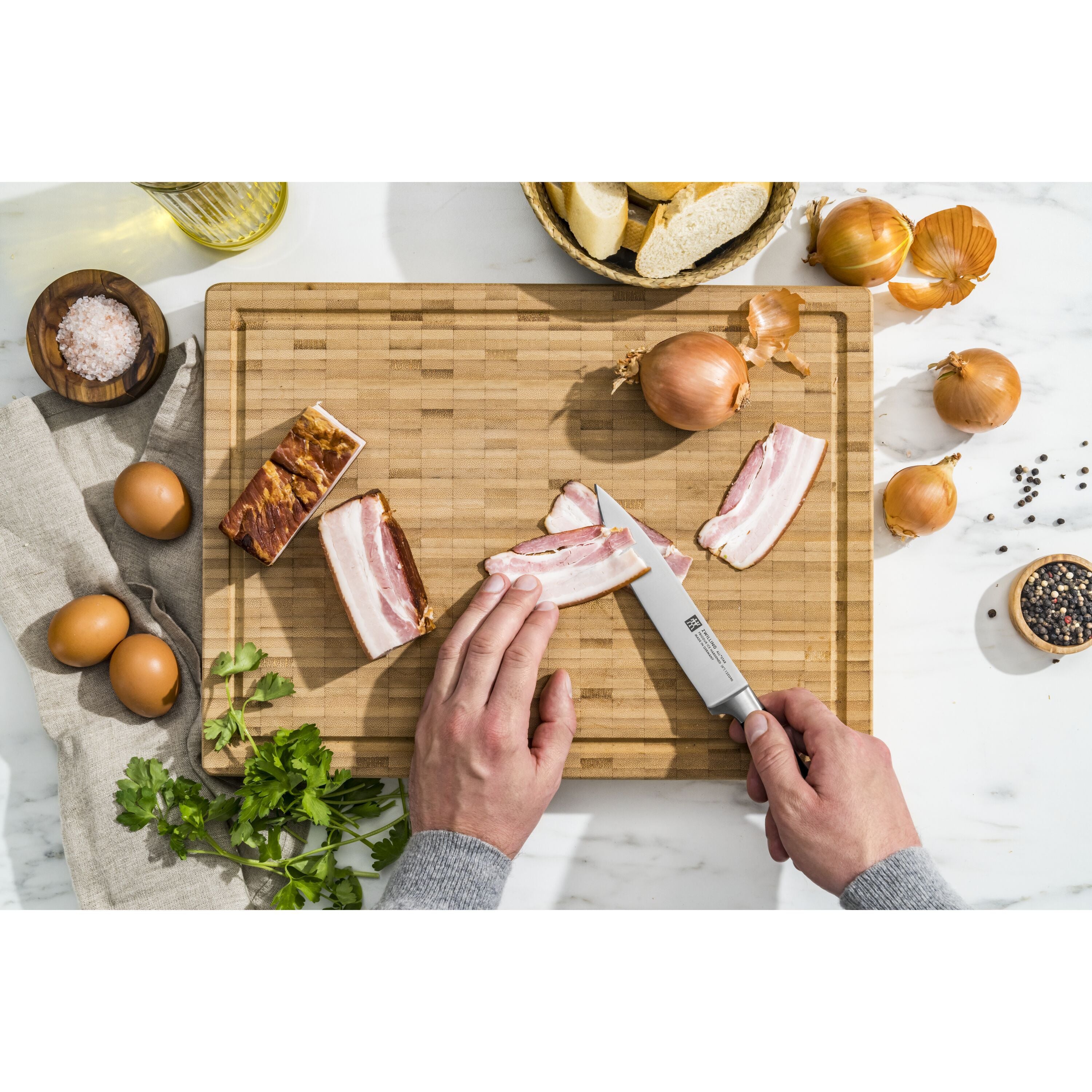 Person cutting bacon on a wooden cutting board with various ingredients around.