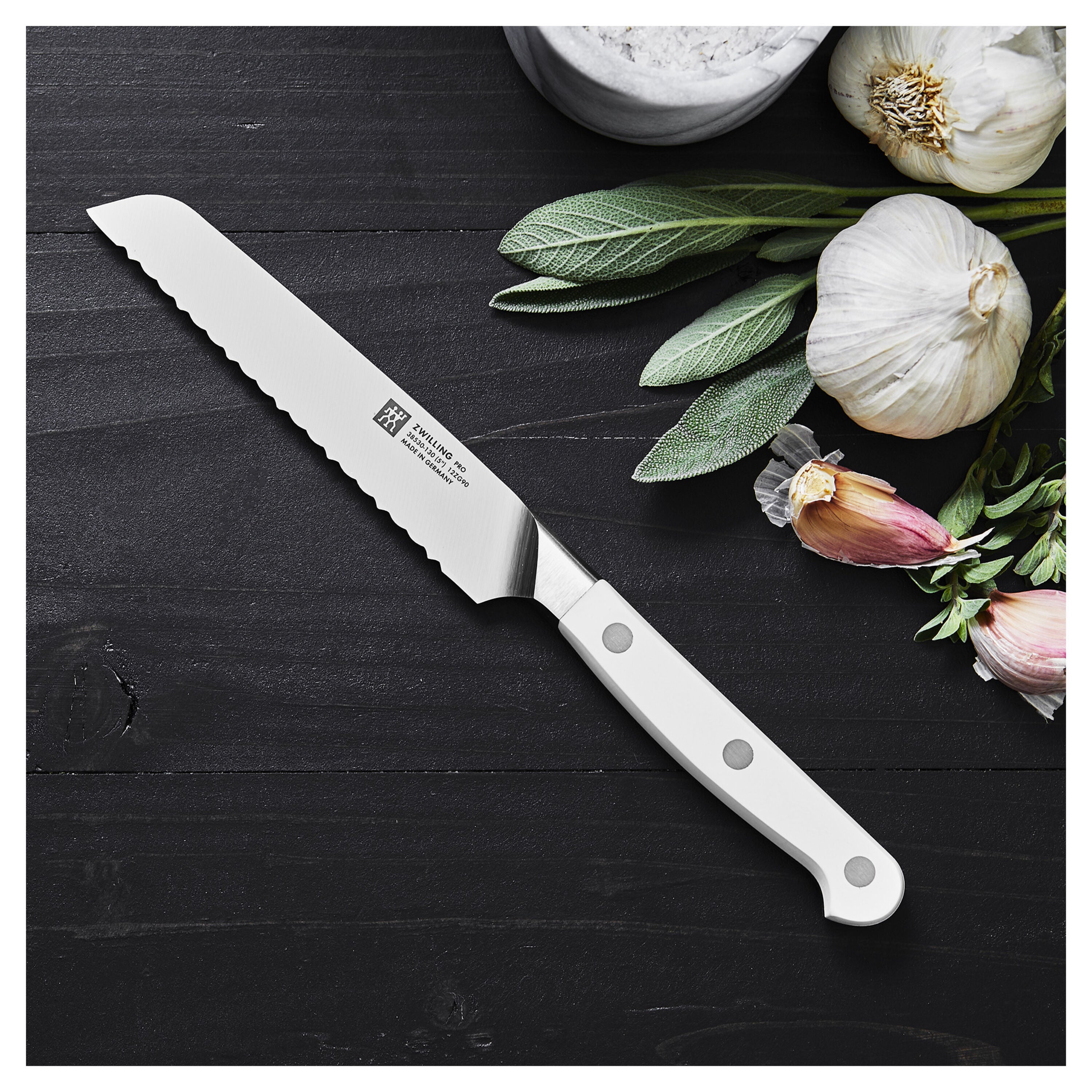 Serrated knife on a dark wooden surface with garlic and leaves.