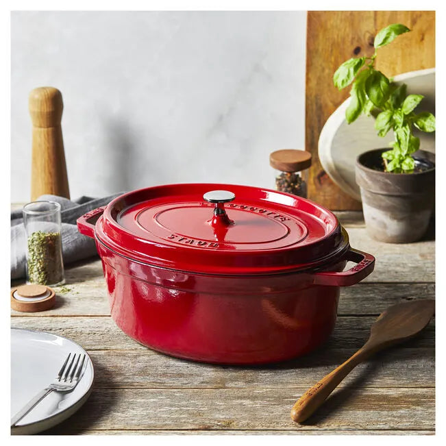 Red cast iron cookware on a wooden table with kitchen items in the background
