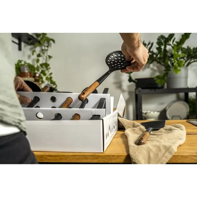 Person assembling Staub Silicone Kitchen Utensil Set on countertop, featuring matte-black silicone and acacia wood handles.