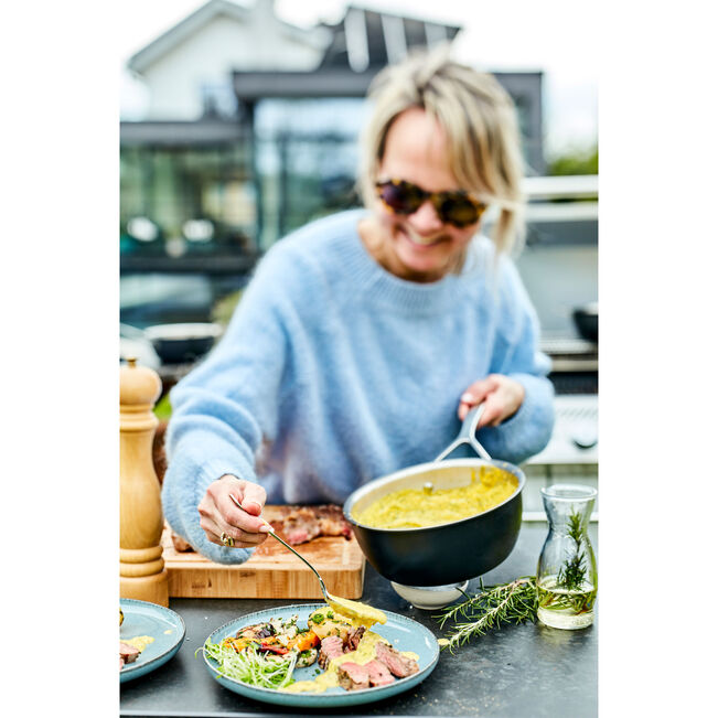 Woman serving food from a pan outdoors with a blurred background