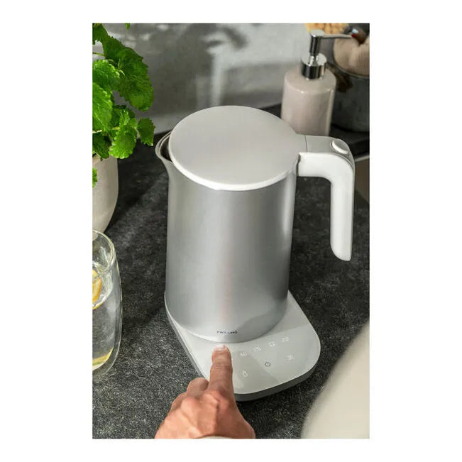 White electric kettle on a kitchen counter with a hand pointing at it.