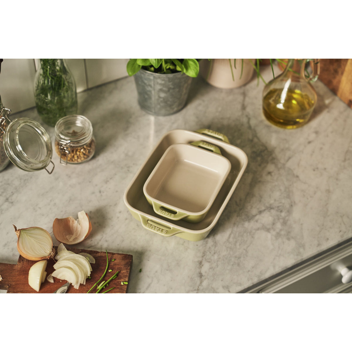 Set of square baking dishes on a kitchen counter with ingredients and utensils.