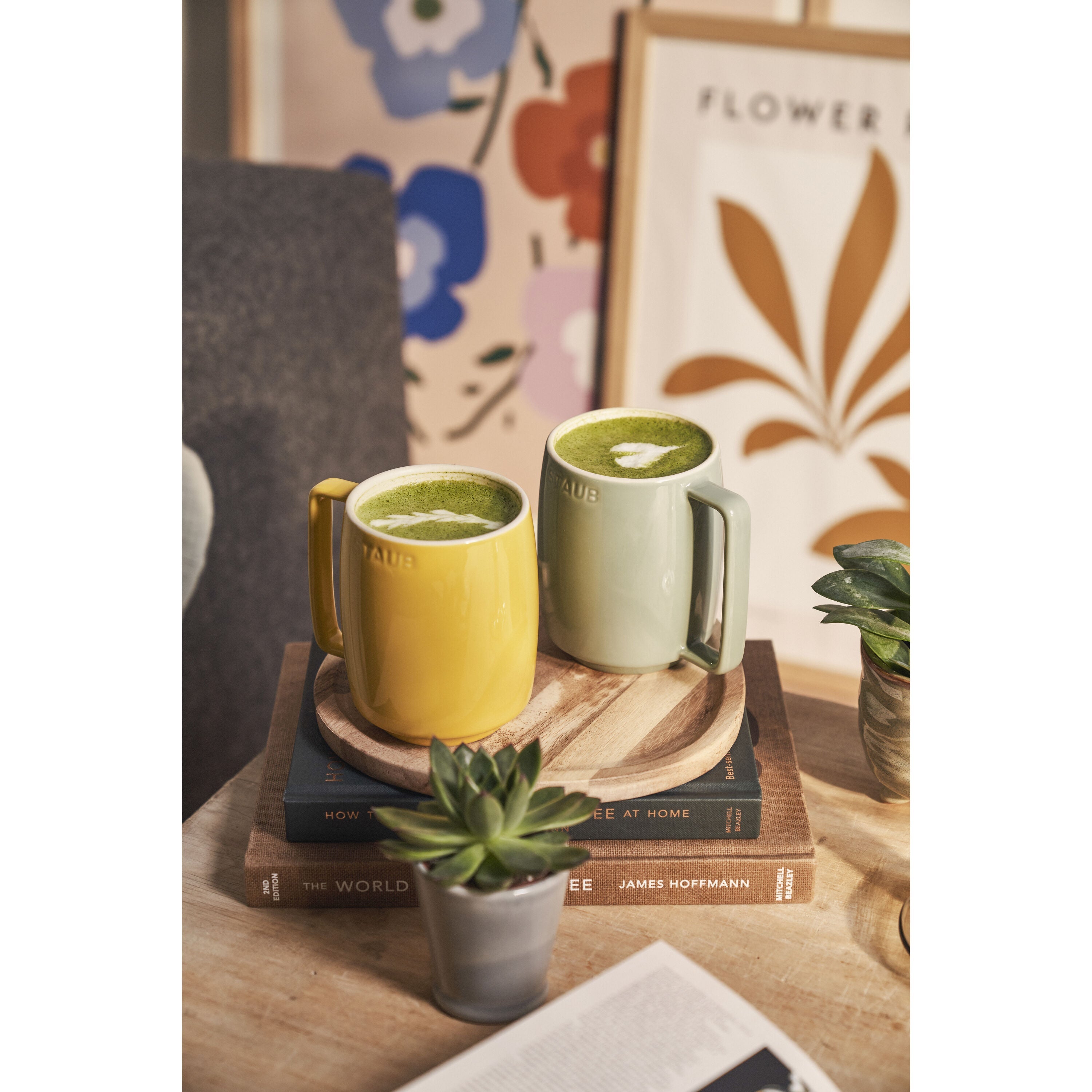 Two mugs of green tea on a wooden tray with books and a plant in a cozy room.