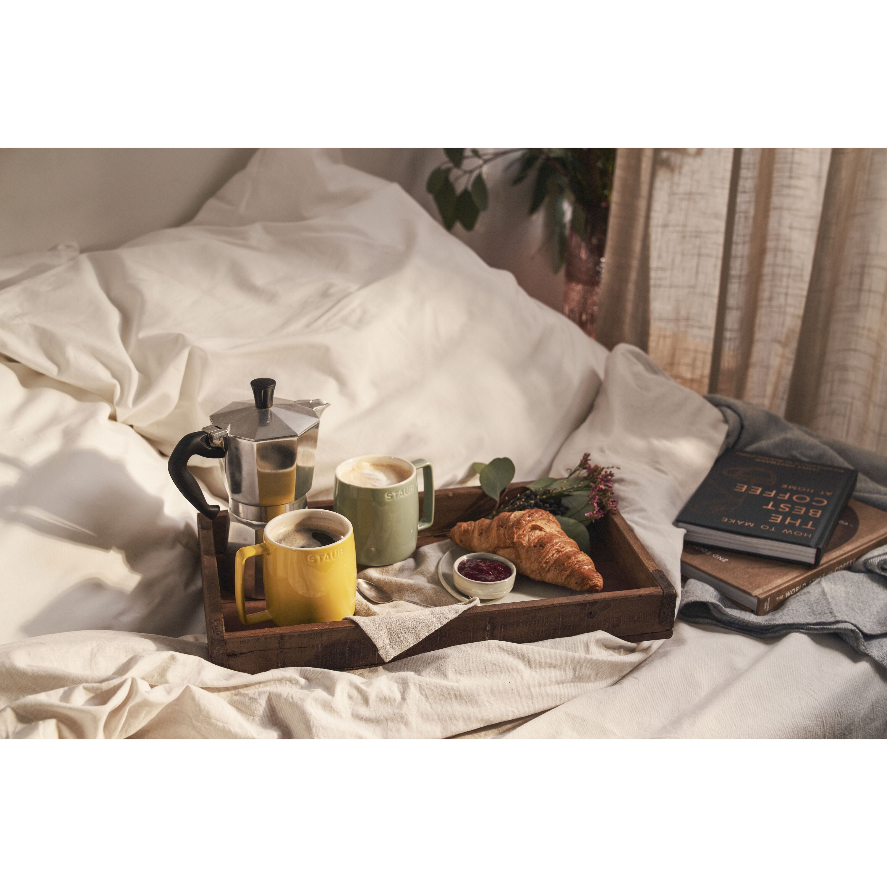Breakfast tray with coffee, croissant, and books on a bed