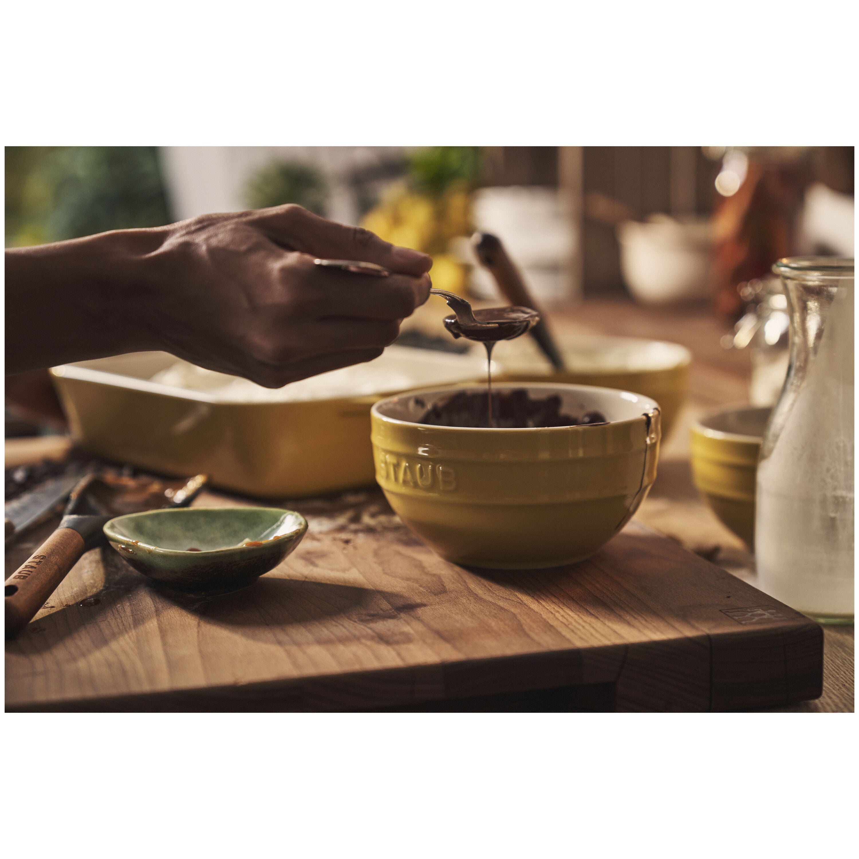 Person pouring liquid into a yellow bowl on a wooden surface with a blurred background