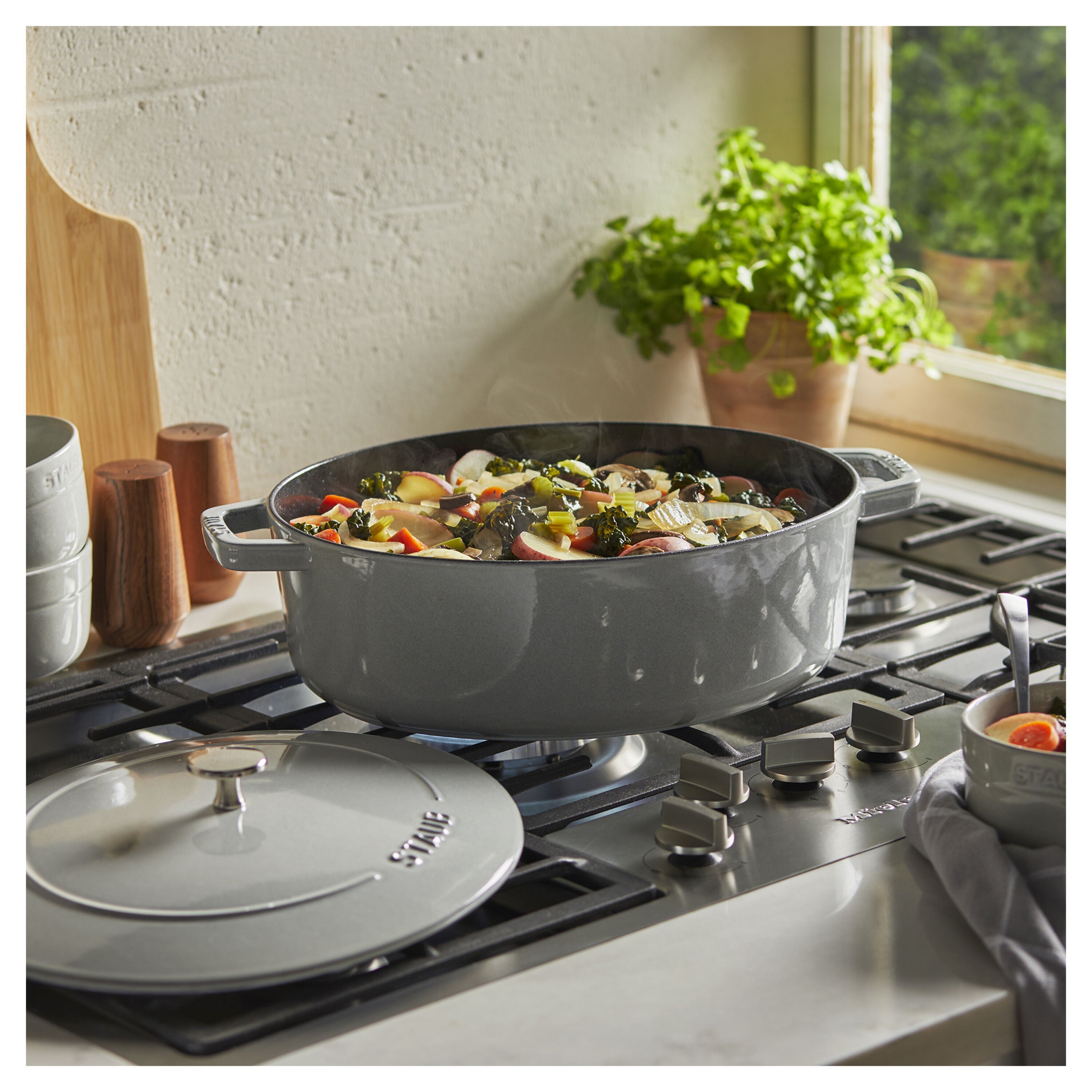 white Staub pot on a stove with vegetables inside, in a kitchen setting.