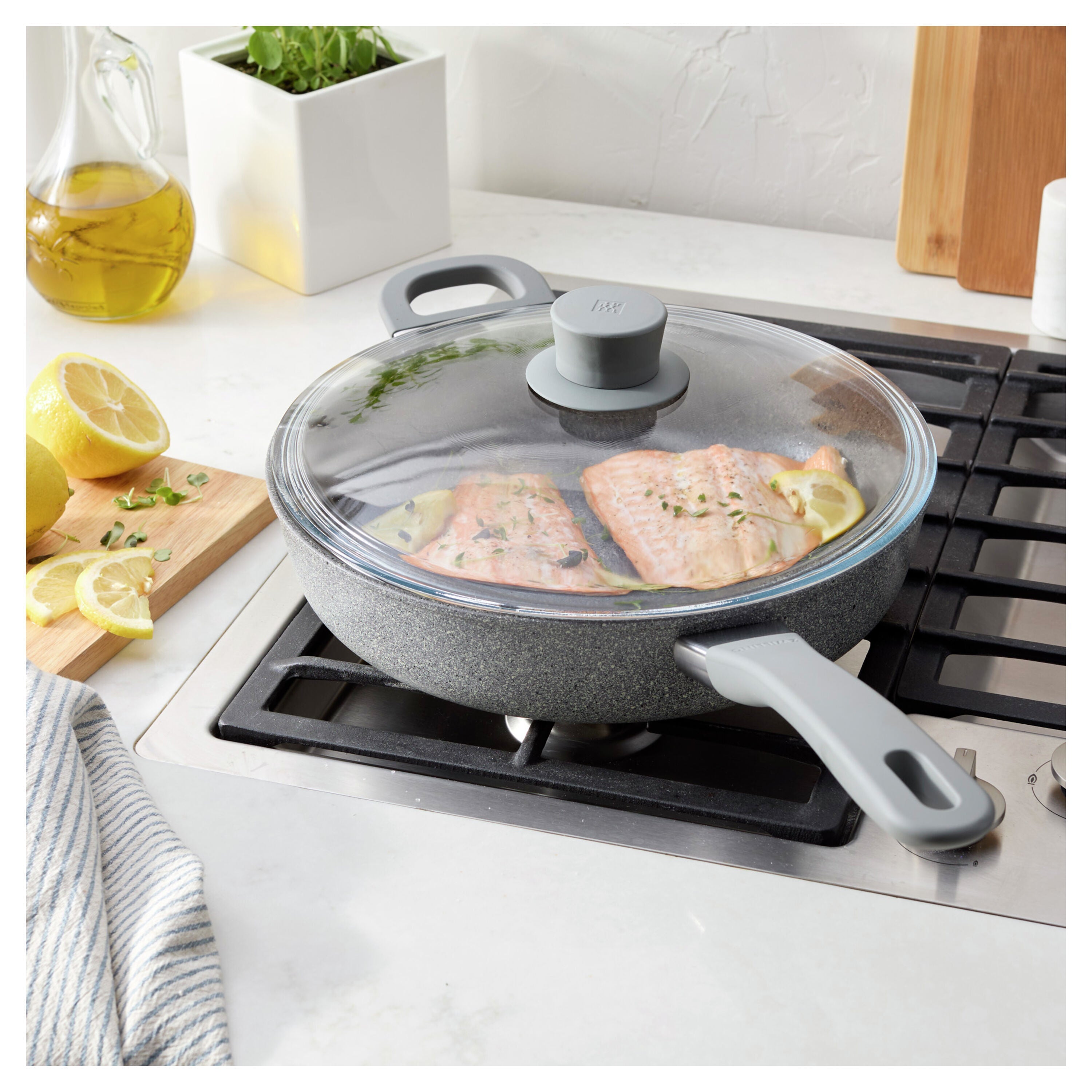 Gray non-stick frying pan with lid on a stove, containing fish fillets.