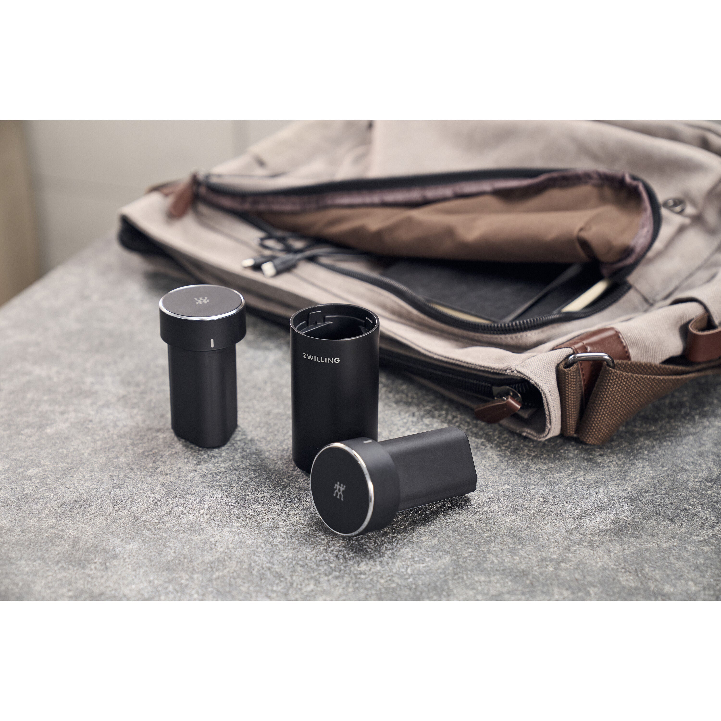 Three black cylindrical objects on a textured surface with a bag in the background