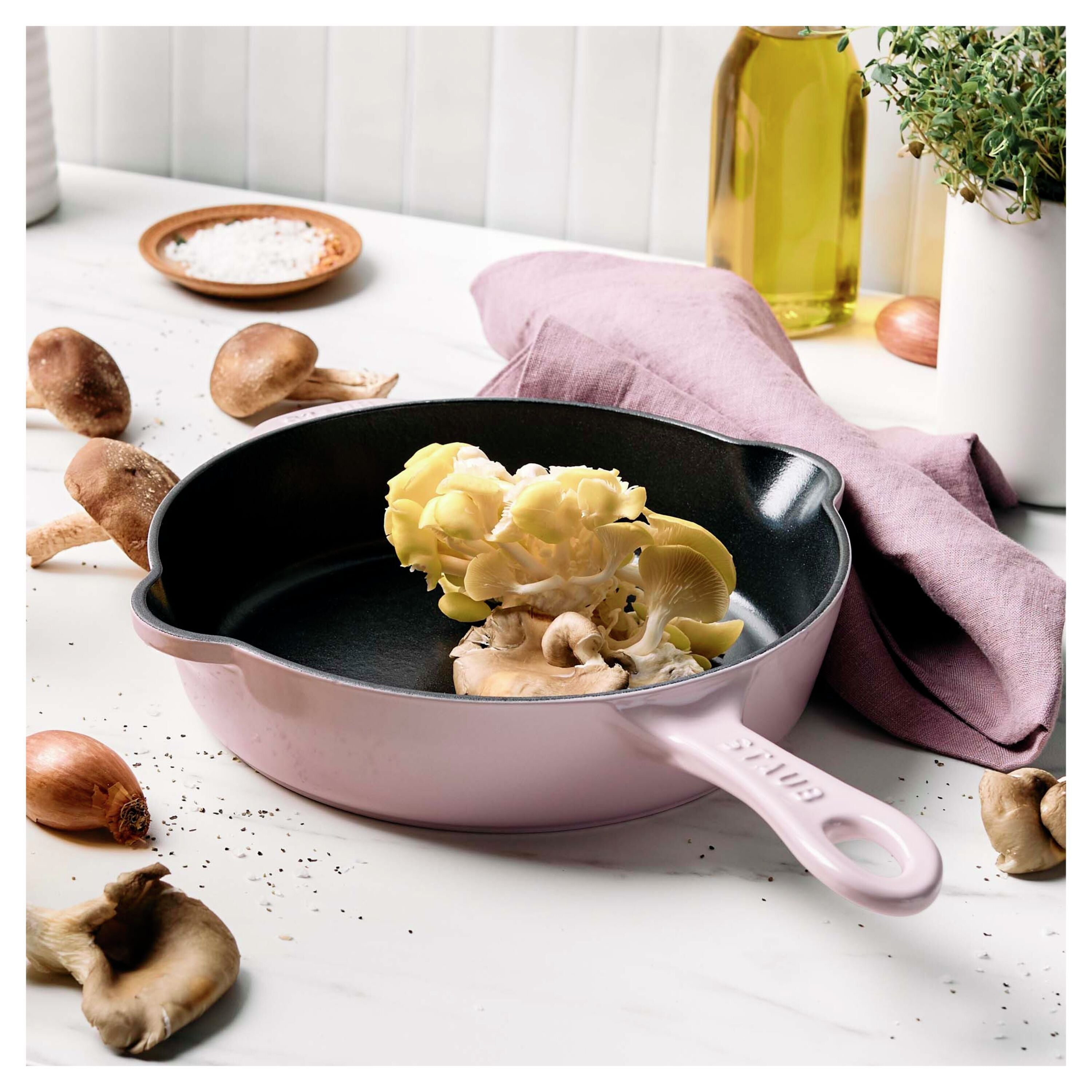 Pink frying pan with vegetables on a white surface